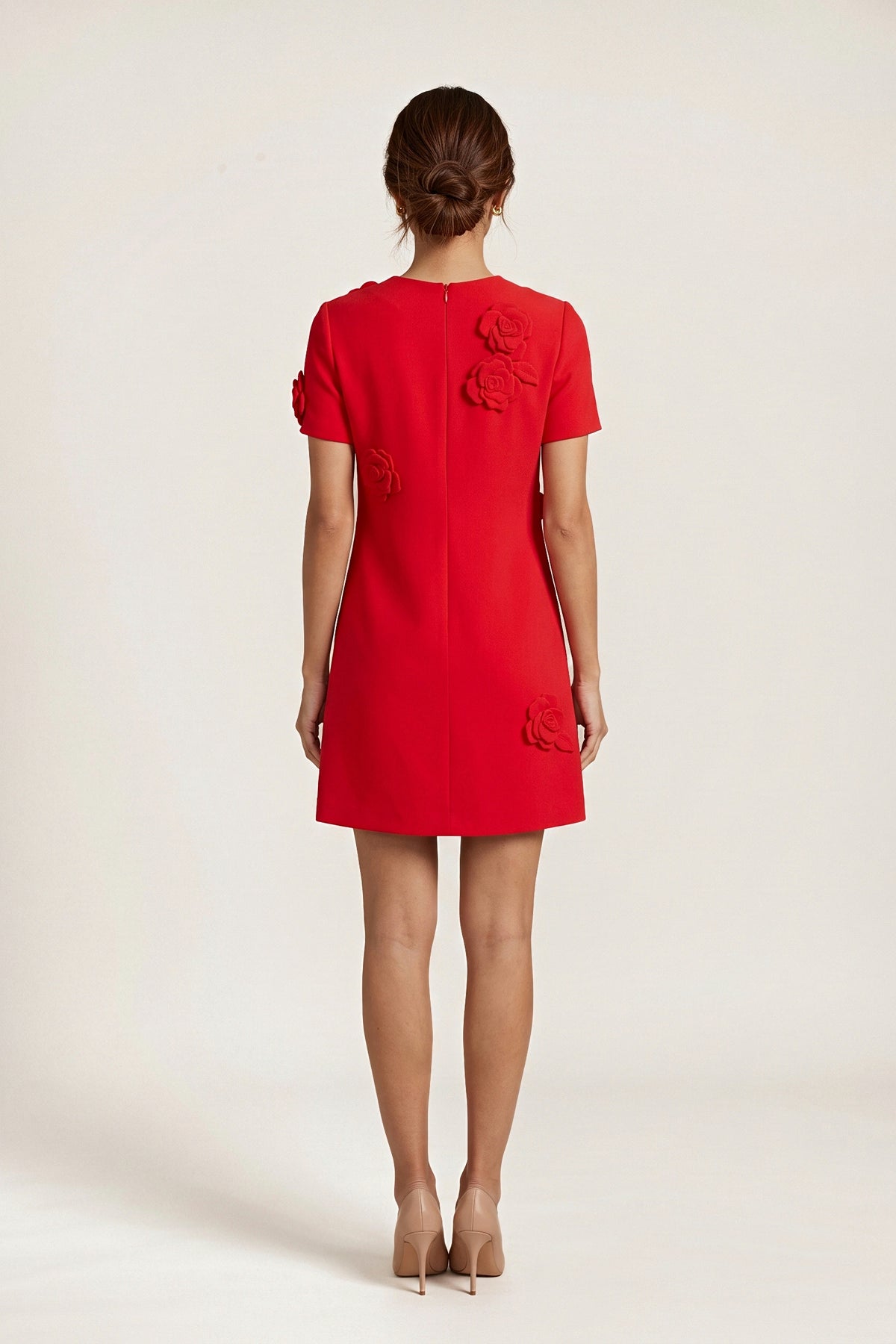 Back view of the red shift dress on a model, with a centre back zip and fabric roses on the upper back and hem.