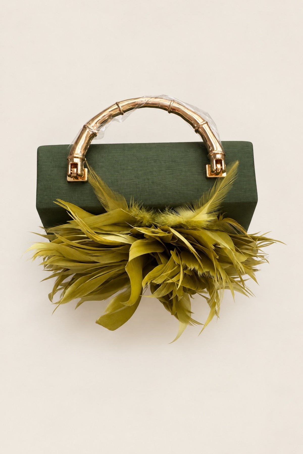 A dark green rectangular handbag with a gold bamboo-style top handle and a large olive-green feather embellishment in front, photographed on a plain light beige background.