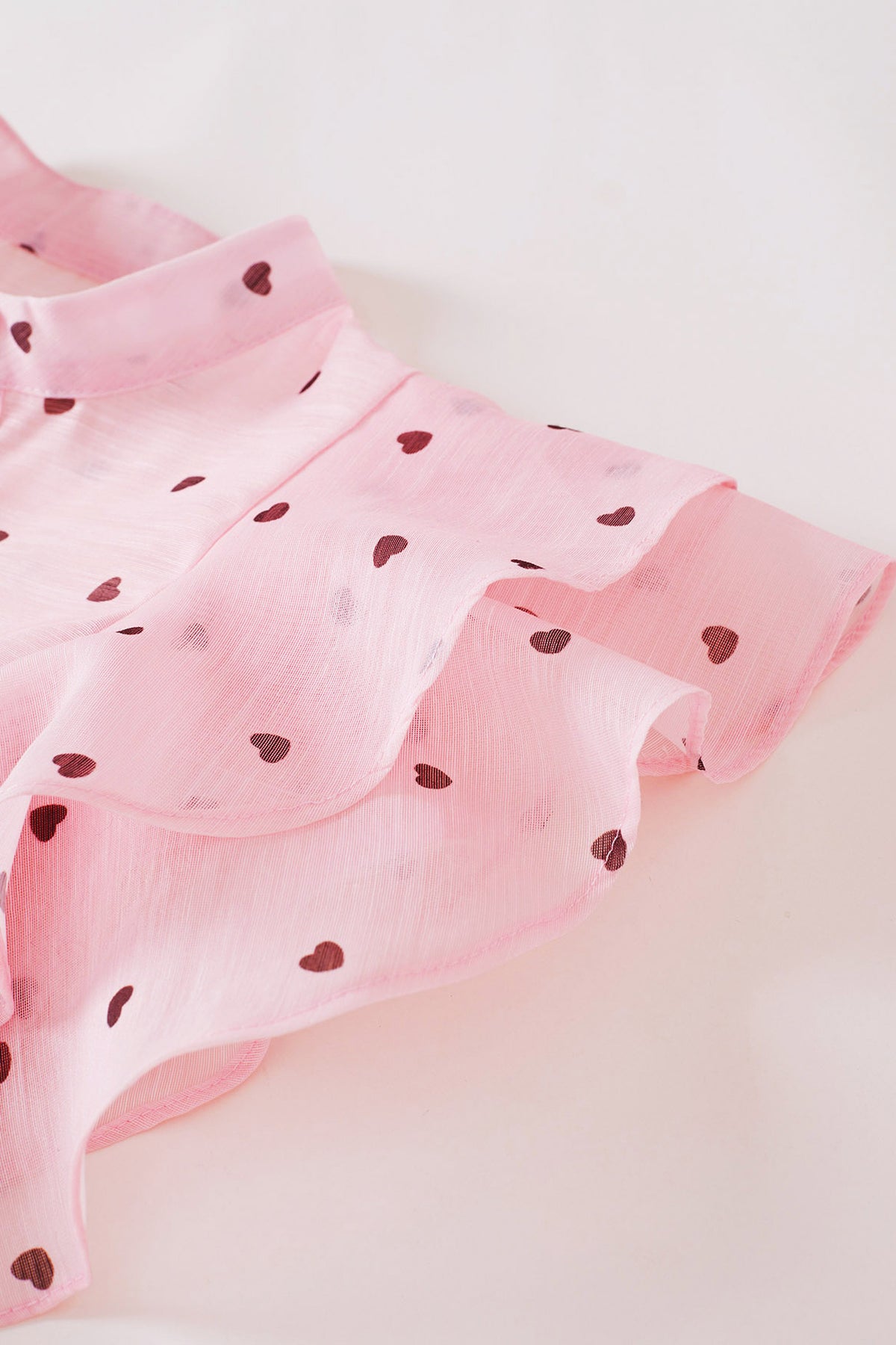 Close-up of the layered organza shoulder ruffle with its scattered burgundy heart print.