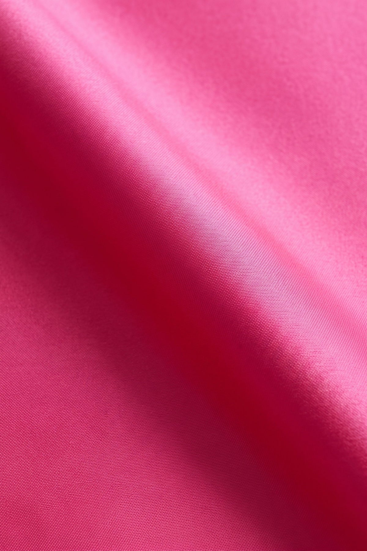 A close-up of bright pink satin or silk fabric with soft diagonal folds and a subtle sheen.