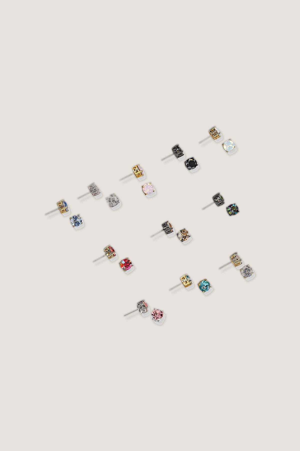 The Impression sparkle stud earrings in all twelve colours, including iridescent coral, laid out on a warm background.
