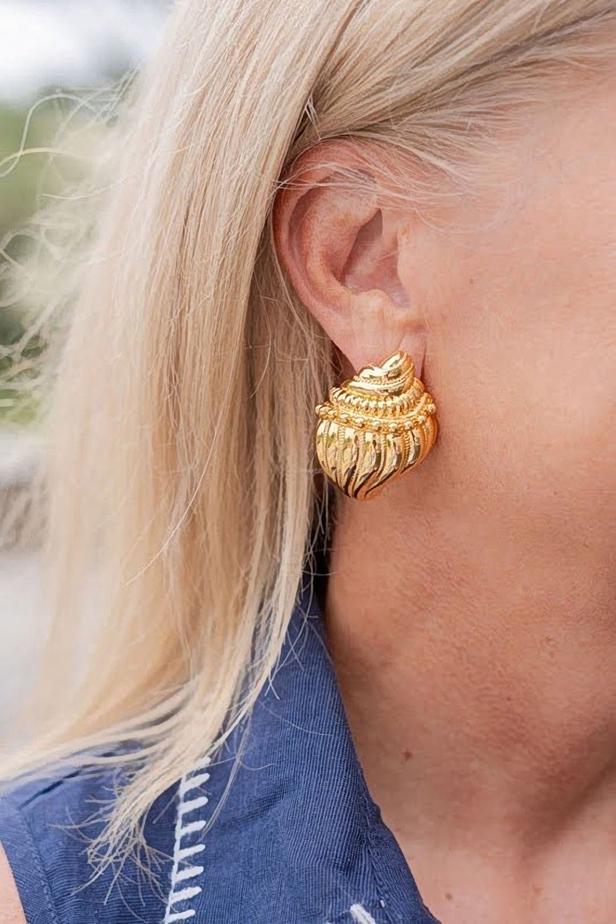 Close-up of the gold James conch shell earring worn on a woman's ear, showing its size against the earlobe.