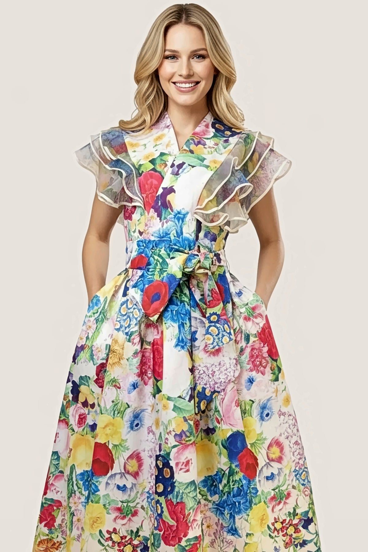 Front view of the Jardin Bloom Dress on a blonde model: wrap V-neckline, tiered organza ruffle cap sleeves with white piped edges, and a self-tie belt tied at the waist.