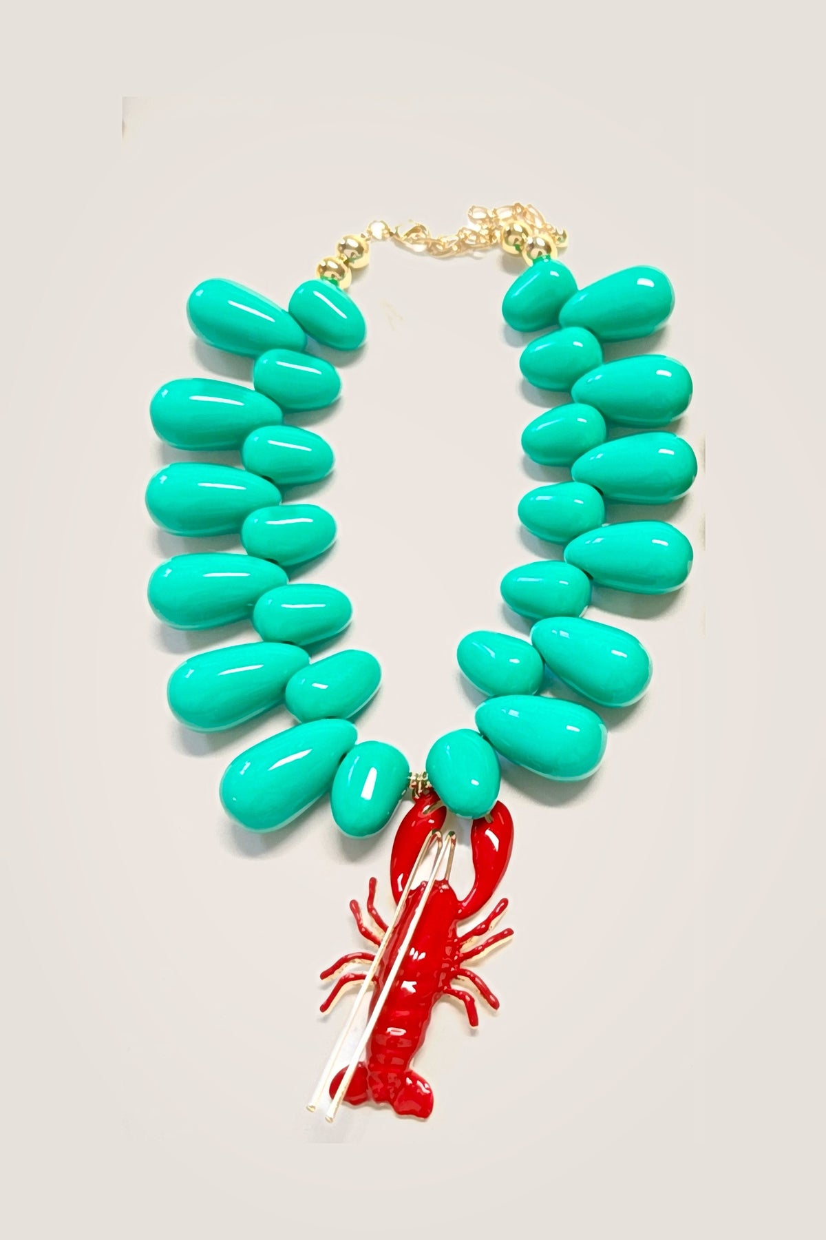 The Lobster Kitsch and Sea necklace laid flat: mint teardrop resin beads with gold bead accents and a red enamel lobster pendant, clasp and extender at the top.