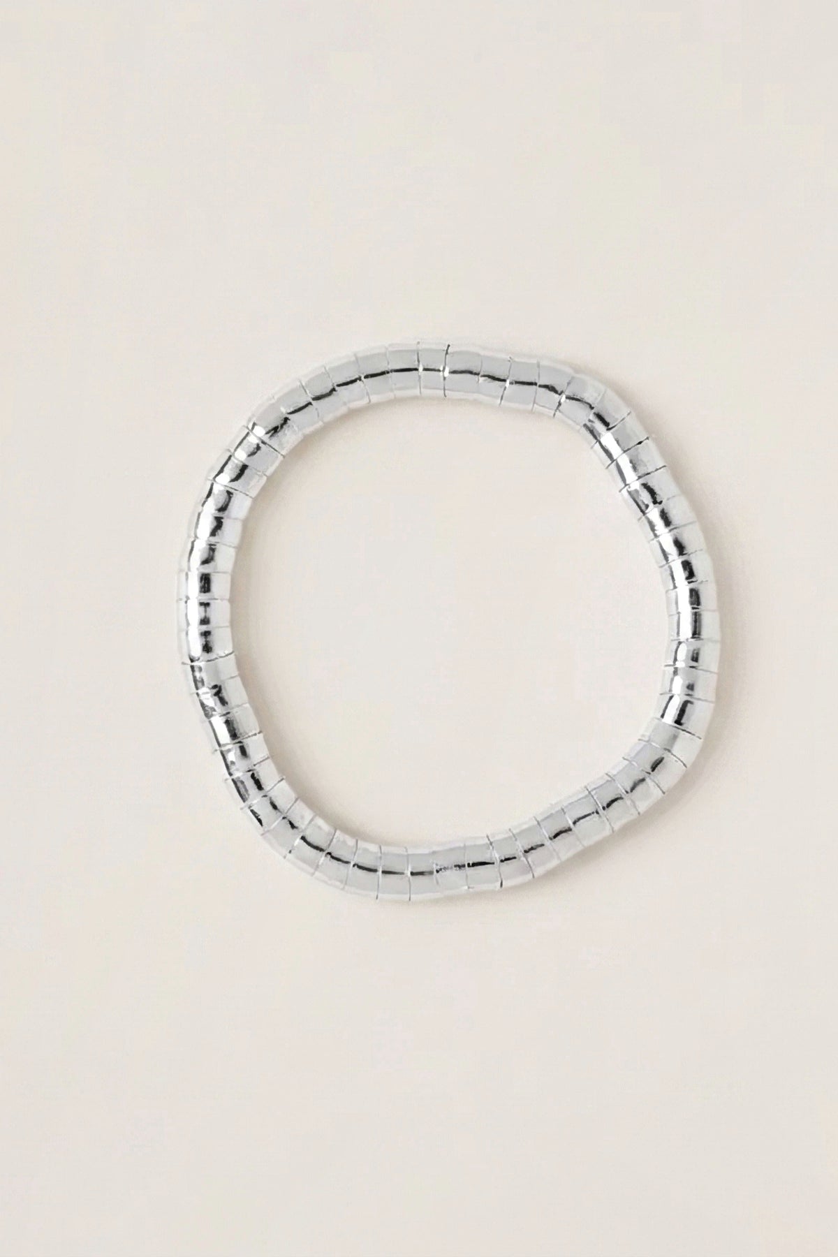Lucille Round Bead Stretch Bracelet in shiny silver-tone plated brass beads, seen from above on a warm greige backdrop.
