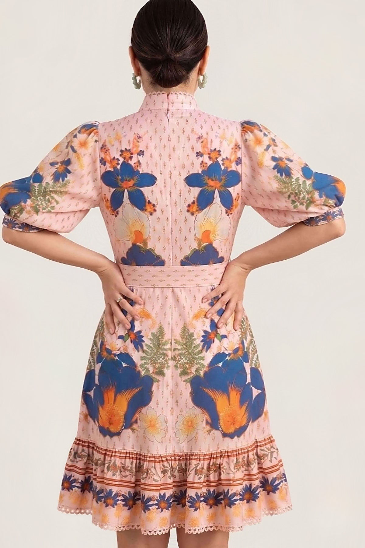 A woman shown from the back wearing a peach dress with blue, orange, and green floral patterns and puff sleeves, photographed against a plain light background.