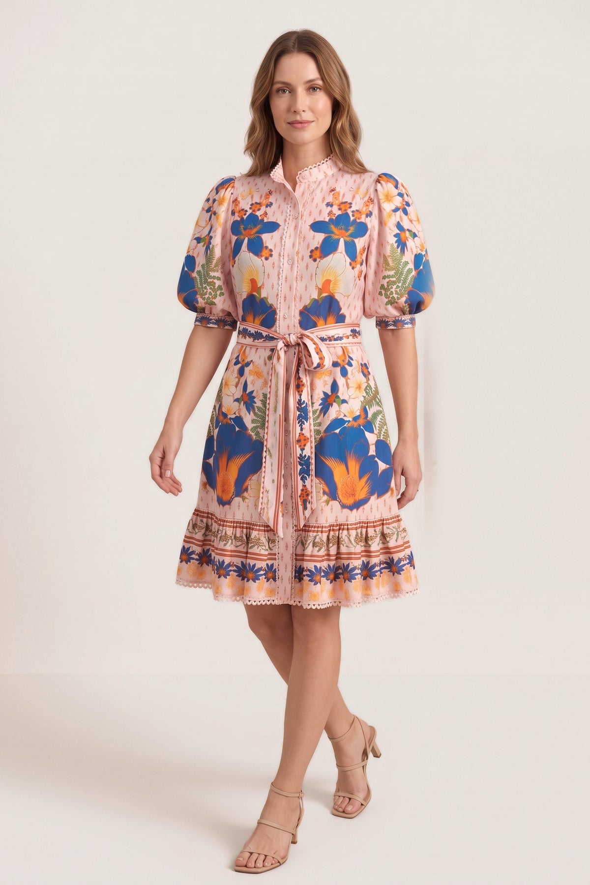 A woman walking in the Marseille Garden Dress in the studio, three-quarter view, showing the stand collar, puff sleeves, tie belt and ruffled border-print hem