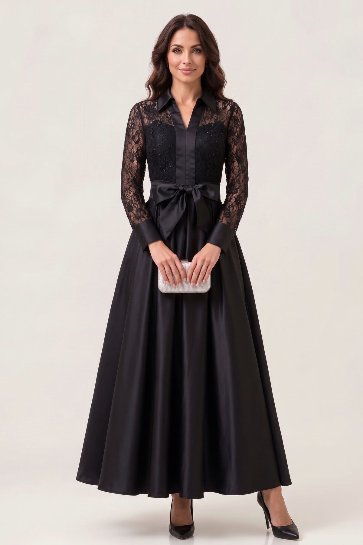 A woman in the Midnight Romance Beaded Lace Maxi Dress facing the camera in the studio, holding a silver clutch, showing the sheer lace sleeves, satin collar and placket, satin bow and full satin skirt