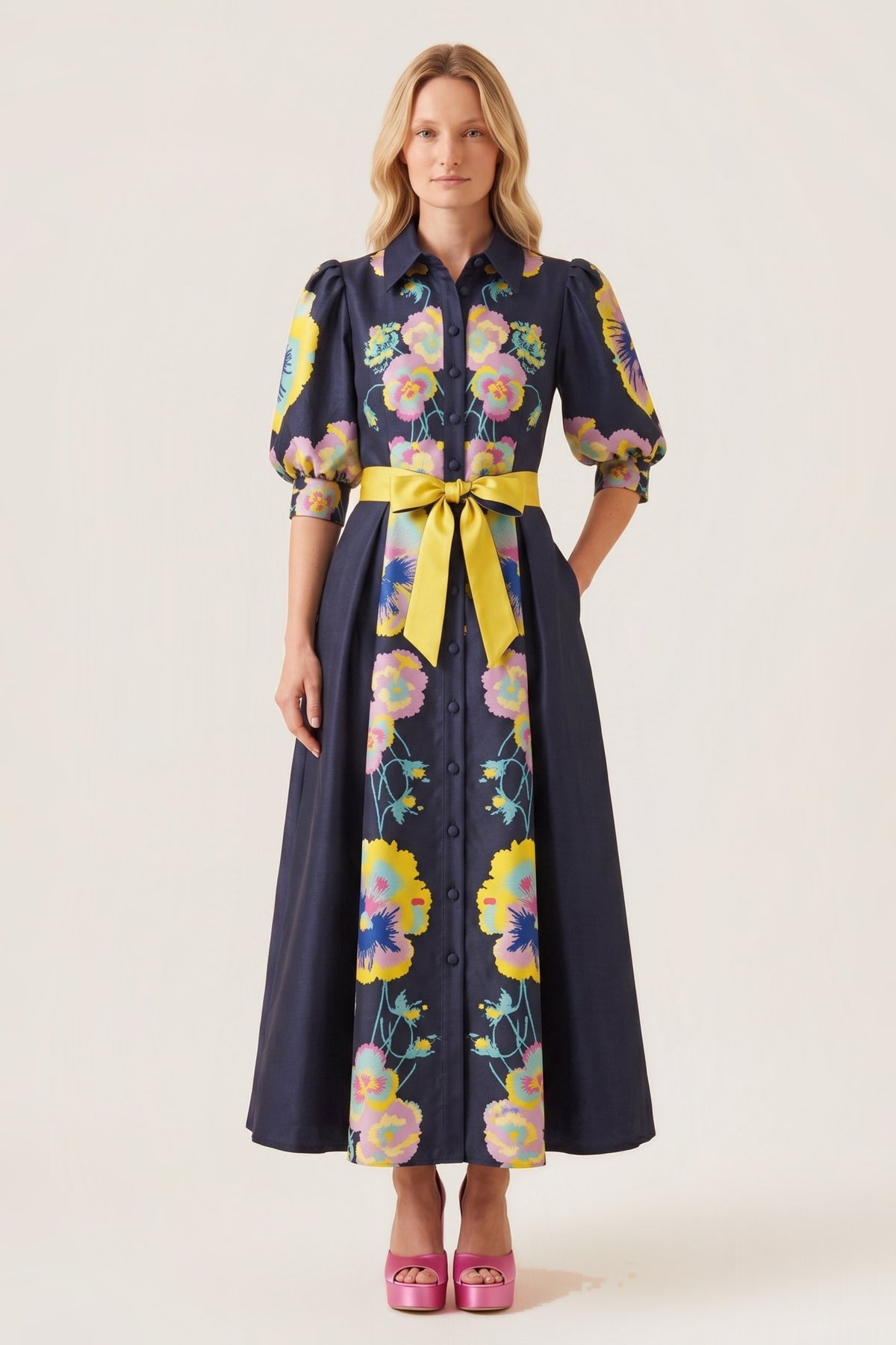 A woman modeling a midnight  blue midi dress with a vibrant multicolor floral print, featuring puff sleeves, a button-down front, and a contrasting yellow tie belt at the waist.