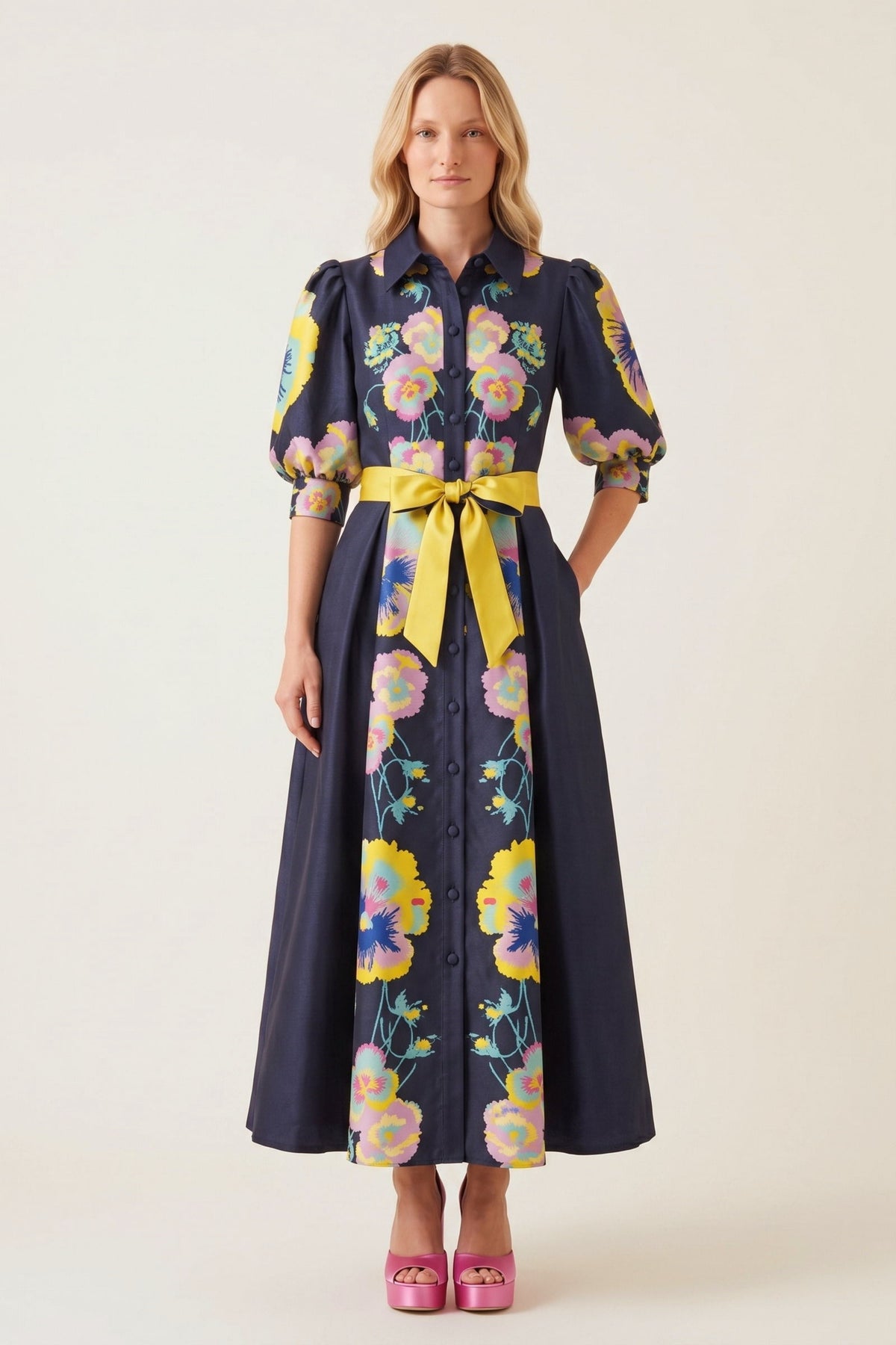 A woman modeling a midnight  blue midi dress with a vibrant multicolor floral print, featuring puff sleeves, a button-down front, and a contrasting yellow tie belt at the waist.