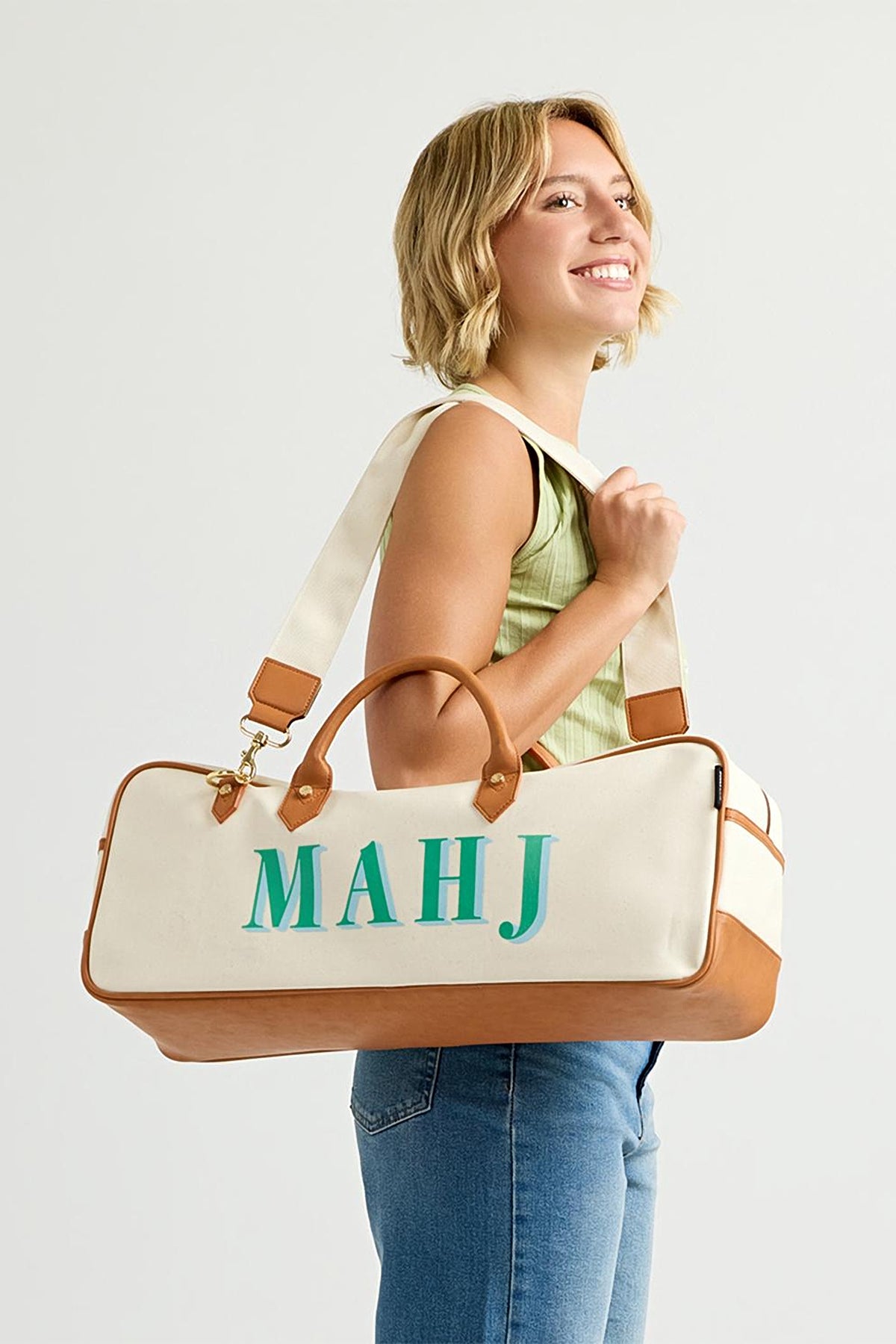 A woman carrying the Mint Margo mahjong tote on her shoulder by its canvas strap, mint MAHJ lettering facing out.