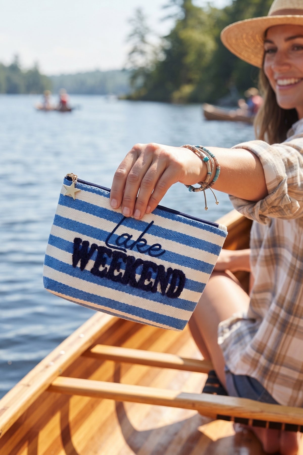 The Morgan "Lake Weekend" zip pouch held up by a woman sitting in a canoe on a lake.