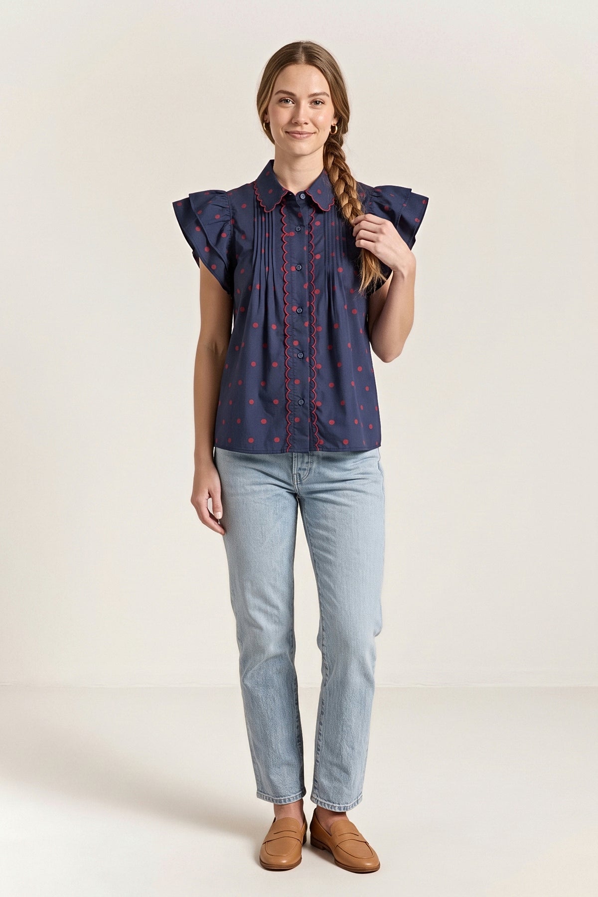 Front view of the navy blouse with small red dots, a red scalloped collar and placket trim and flutter sleeves.