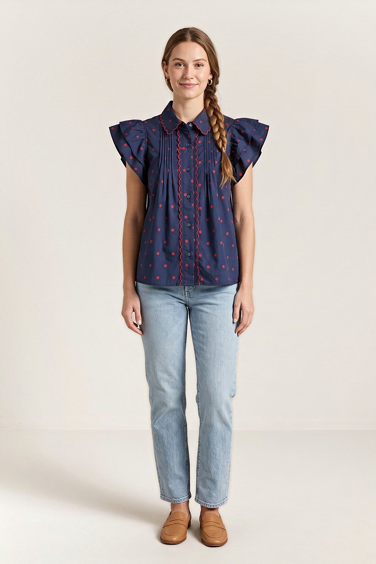 Front view of the navy blouse with small red dots, a red scalloped collar and placket trim and flutter sleeves.