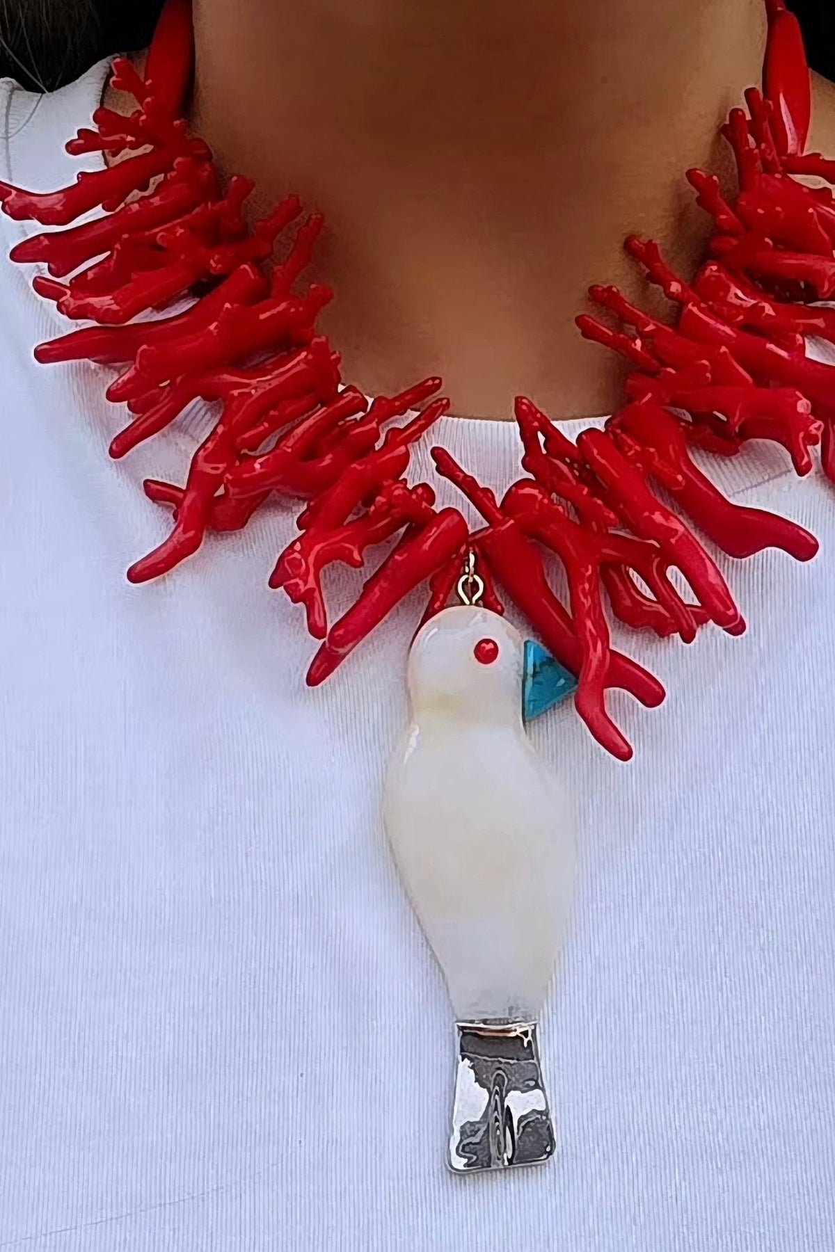 Model in a white tee wearing the Polly Bird and Sea statement necklace, red branch coral beads with a white bird pendant.