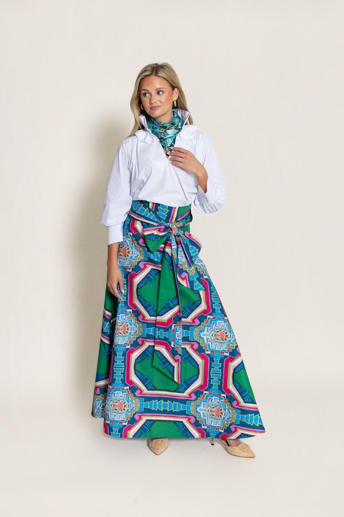 A woman in the Portico Brady wrap maxi skirt with a white shirt and matching Portico print neck scarf, three-quarter view, on a warm neutral studio background.