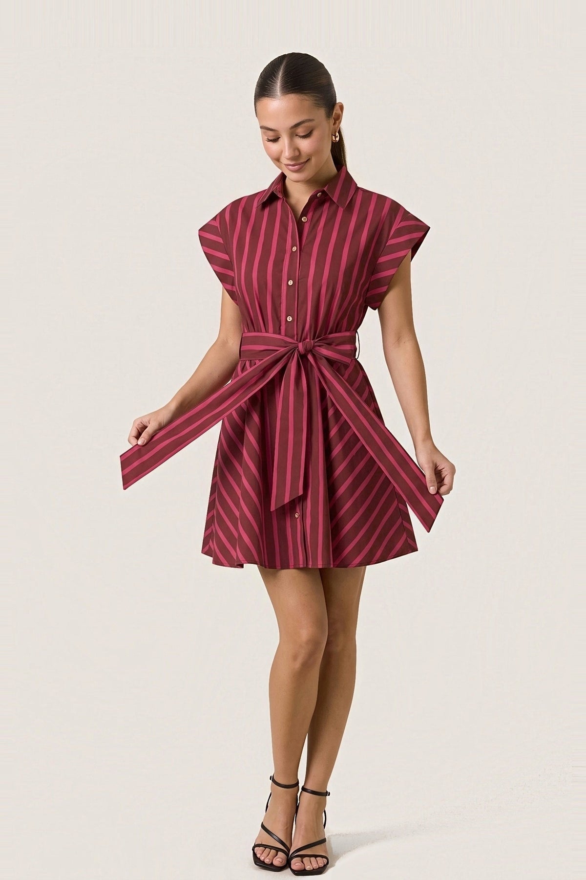 The Raspberry Ribbon striped mini shirt dress, holding out the long ends of the front tie sash.