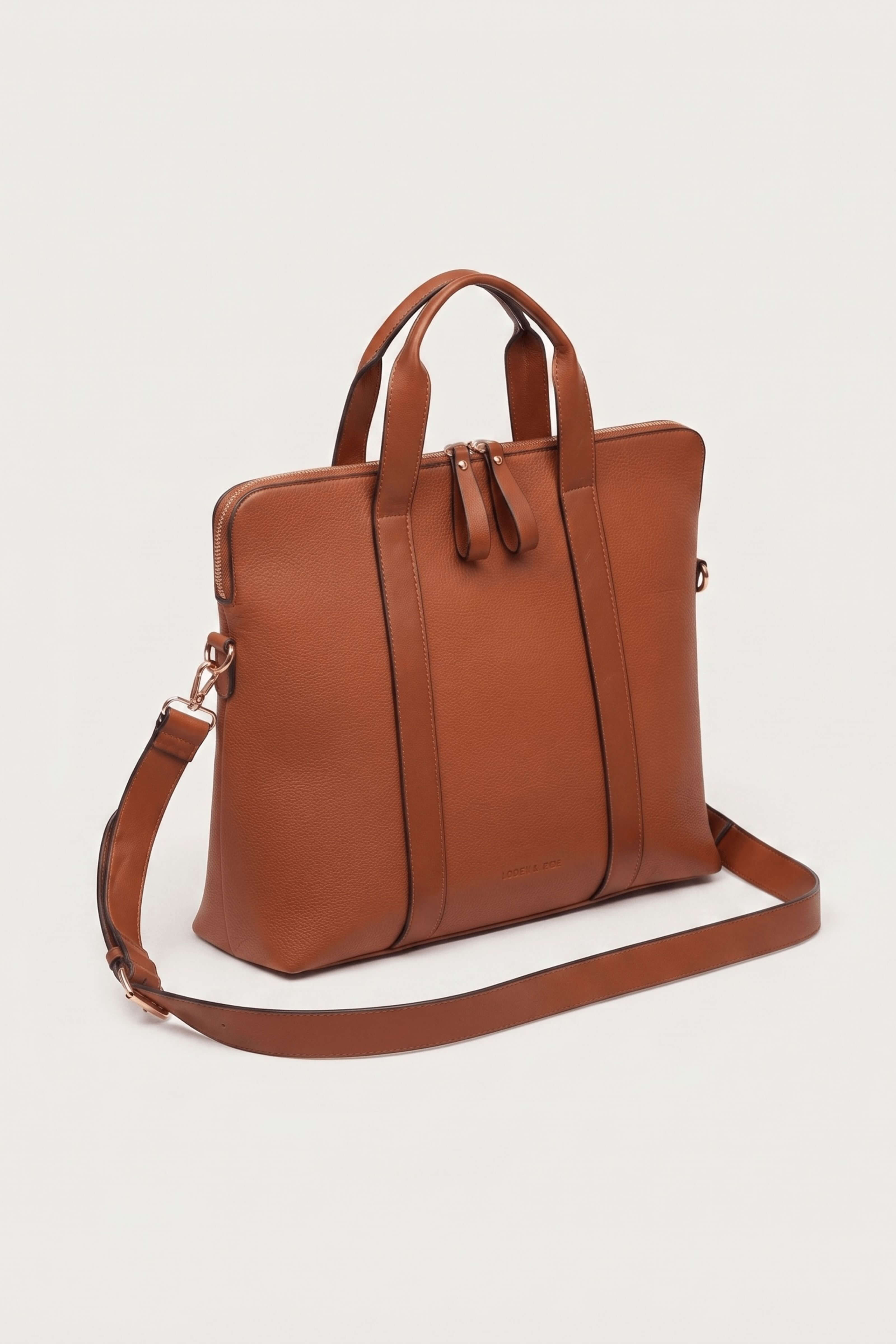 A brown leather tote bag with dual top handles, a detachable shoulder strap, and a zip-top closure, photographed on a clean off-white background.
