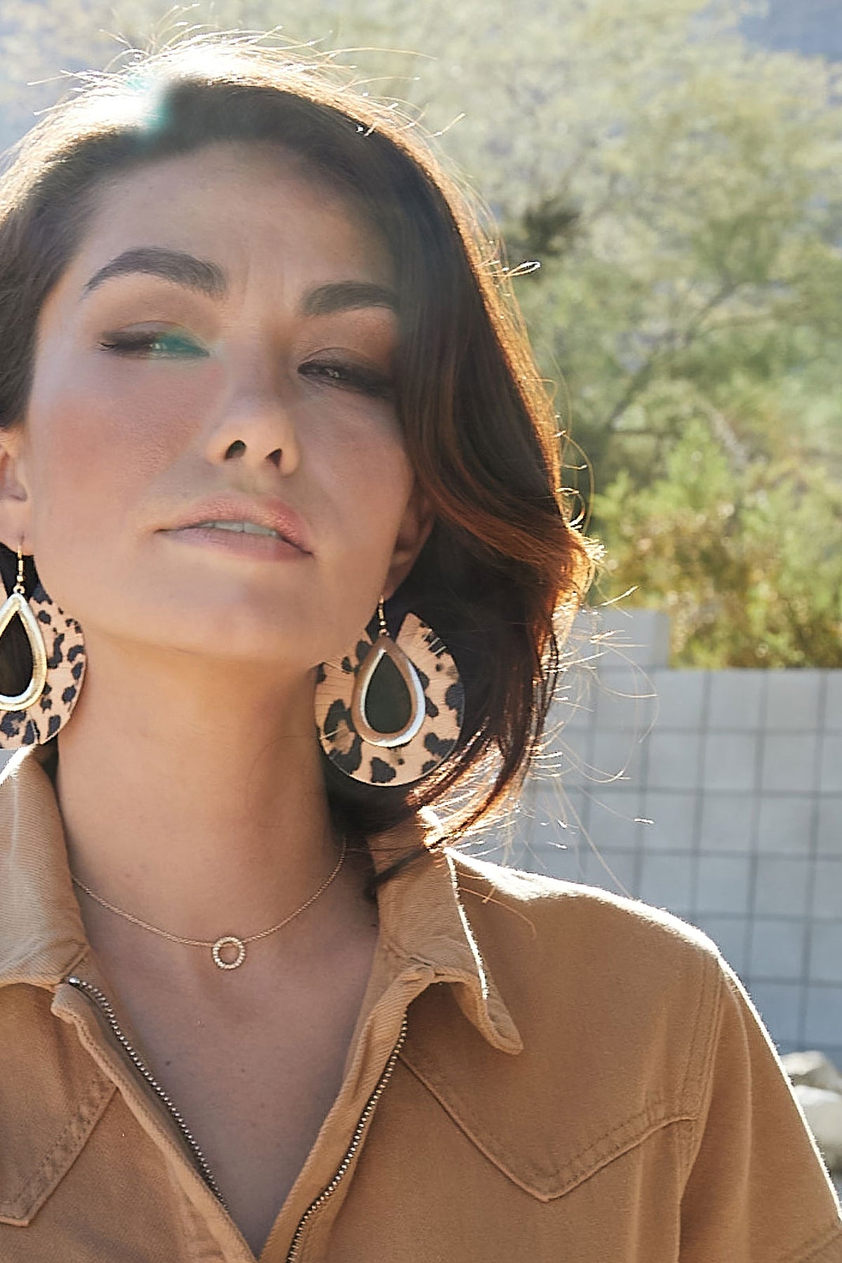 Model in a tan shirt wearing the gold Roo Necklace, a pave crystal circle sitting at the base of the throat.