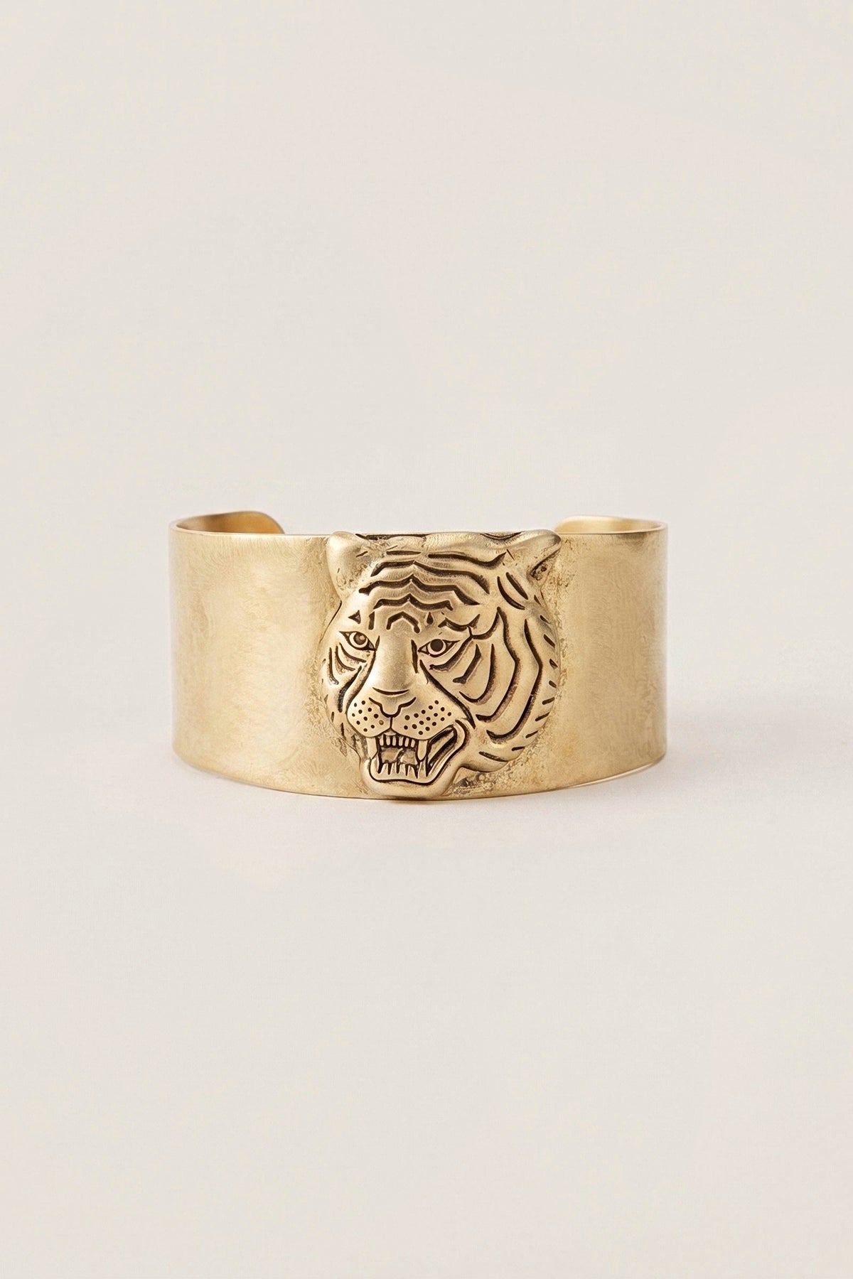 Tarina Tiger Head Cuff in brass with antique gold plating and a sculpted tiger face, on a warm greige backdrop.
