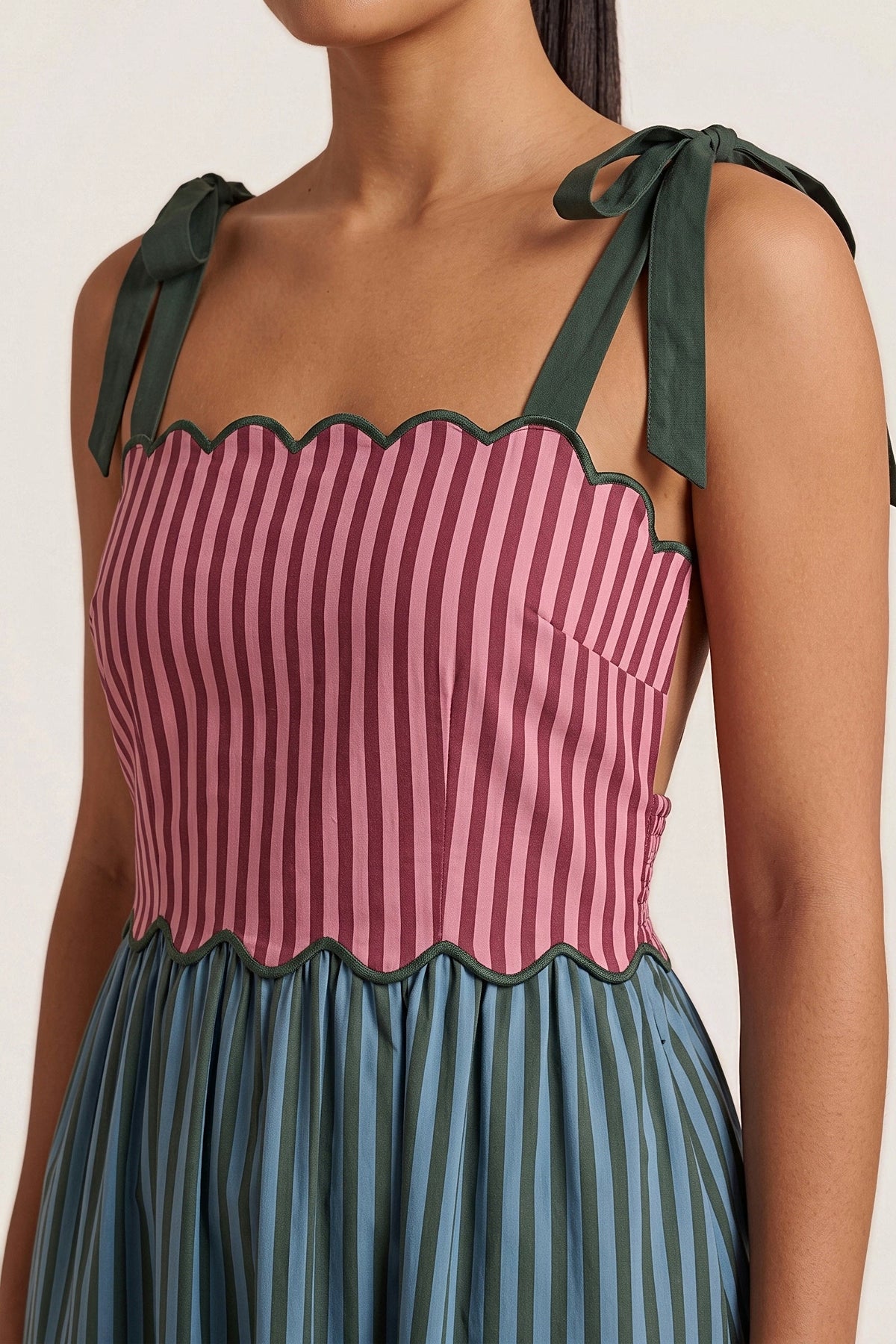 Close-up of the scalloped pink and burgundy striped bodice with green piping and bow tie straps.
