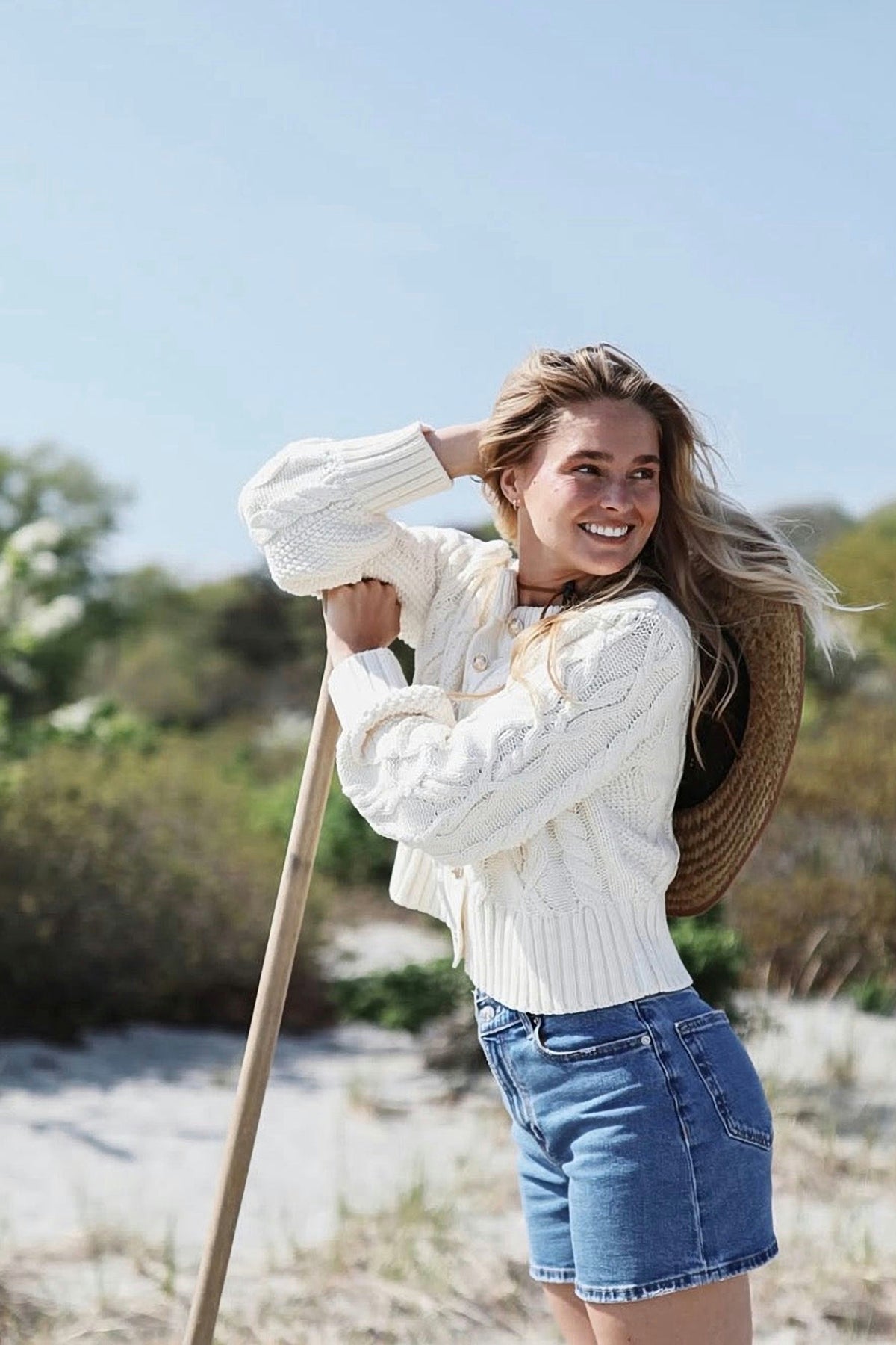 A woman on the beach in the ecru cable knit cardigan and denim shorts.