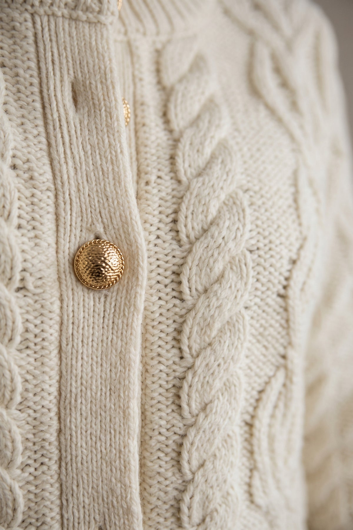 Close-up of the ecru cable knit with a gold shank button and ribbed button band.