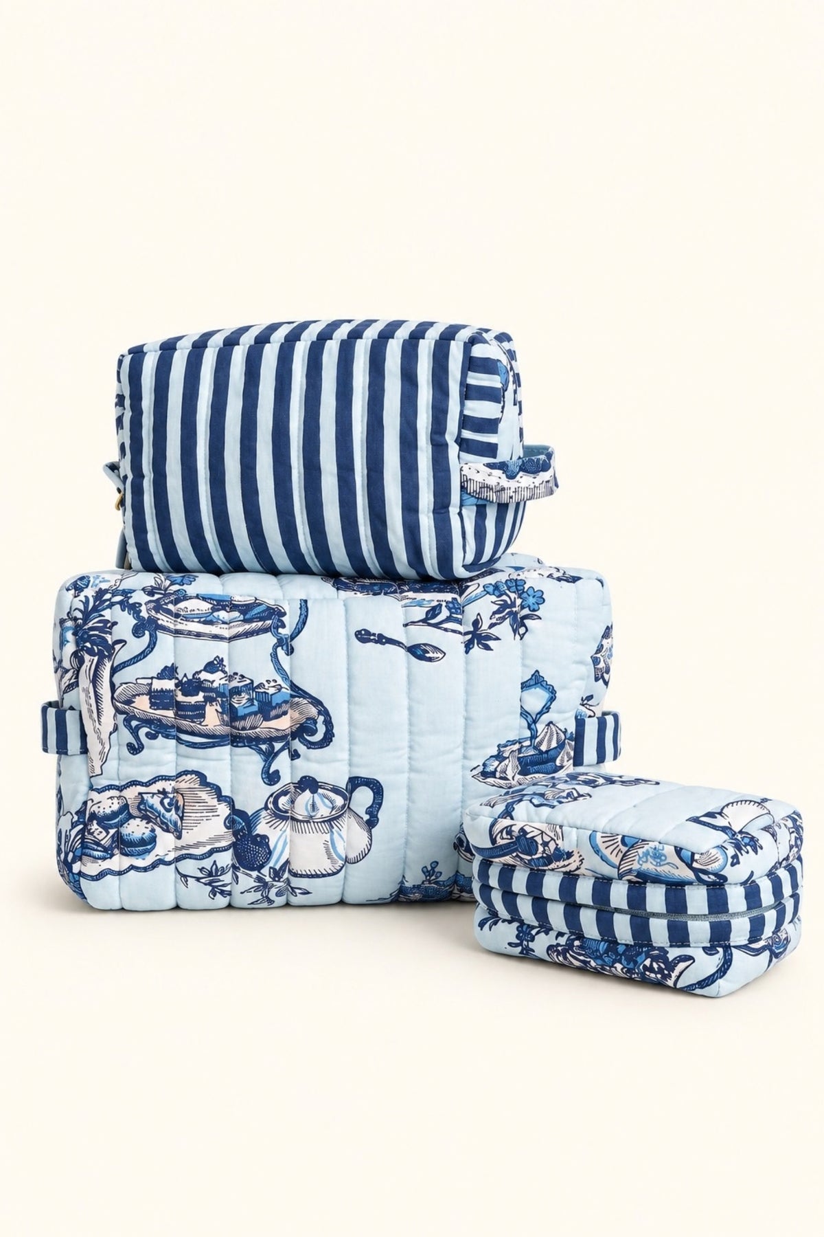 The Three's Best pouch set in blue High Tea toile and navy stripe, three quilted pouches stacked on a white counter.