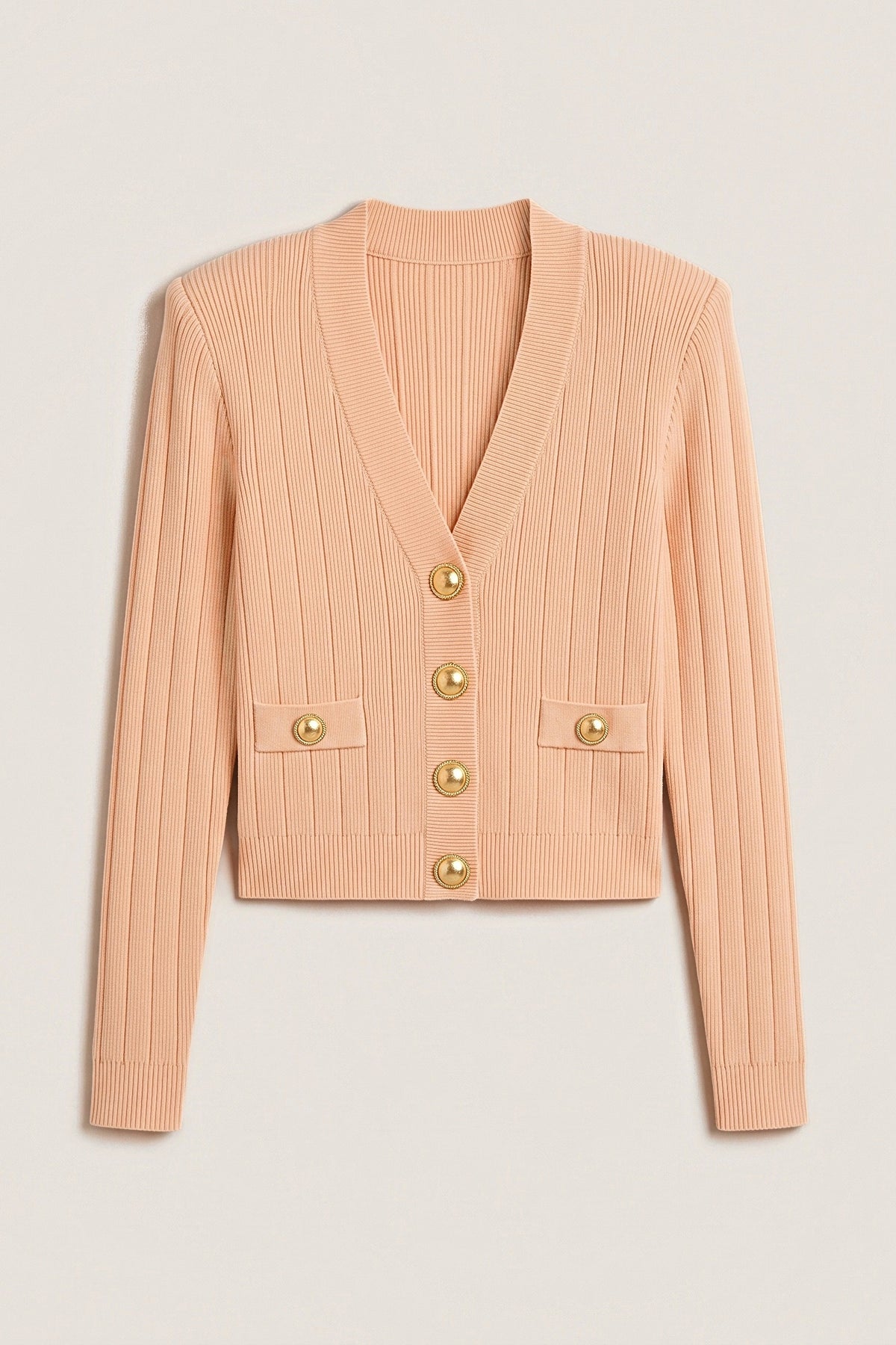 The peach Timeless Knit Cardigan laid flat: cropped ribbed V-neck cardigan with four gold buttons, two button-tab pockets, structured shoulders and ribbed cuffs and hem.