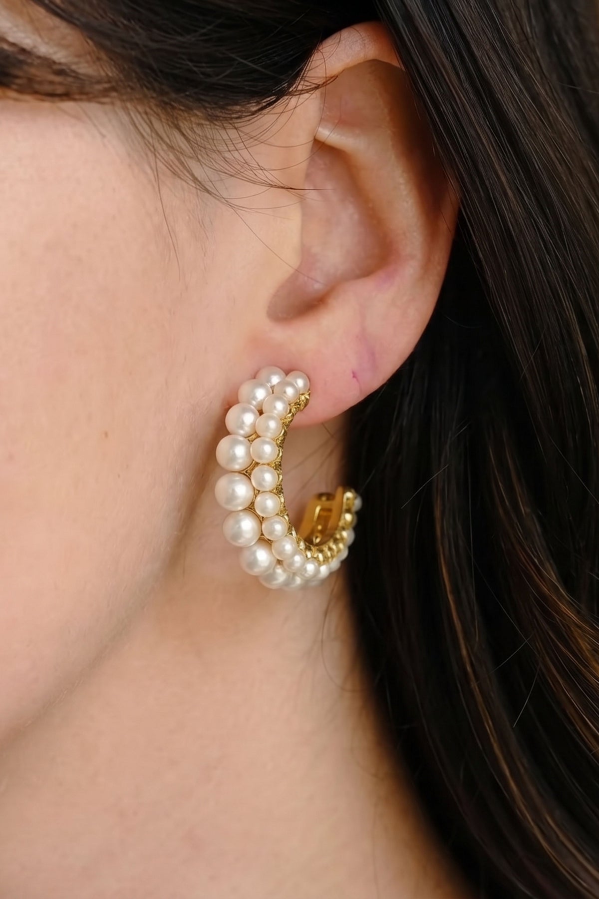 A close-up of a model's ear wearing a gold hoop earring adorned with multiple strands of white faux pearls.