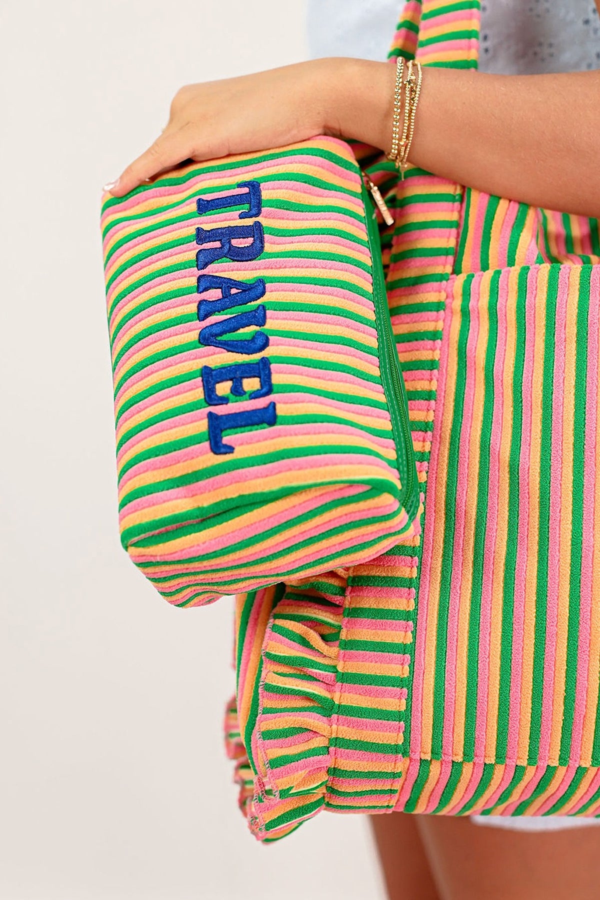 The Travel medium zip pouch in pink and green stripes held in hand, with the matching striped tote.