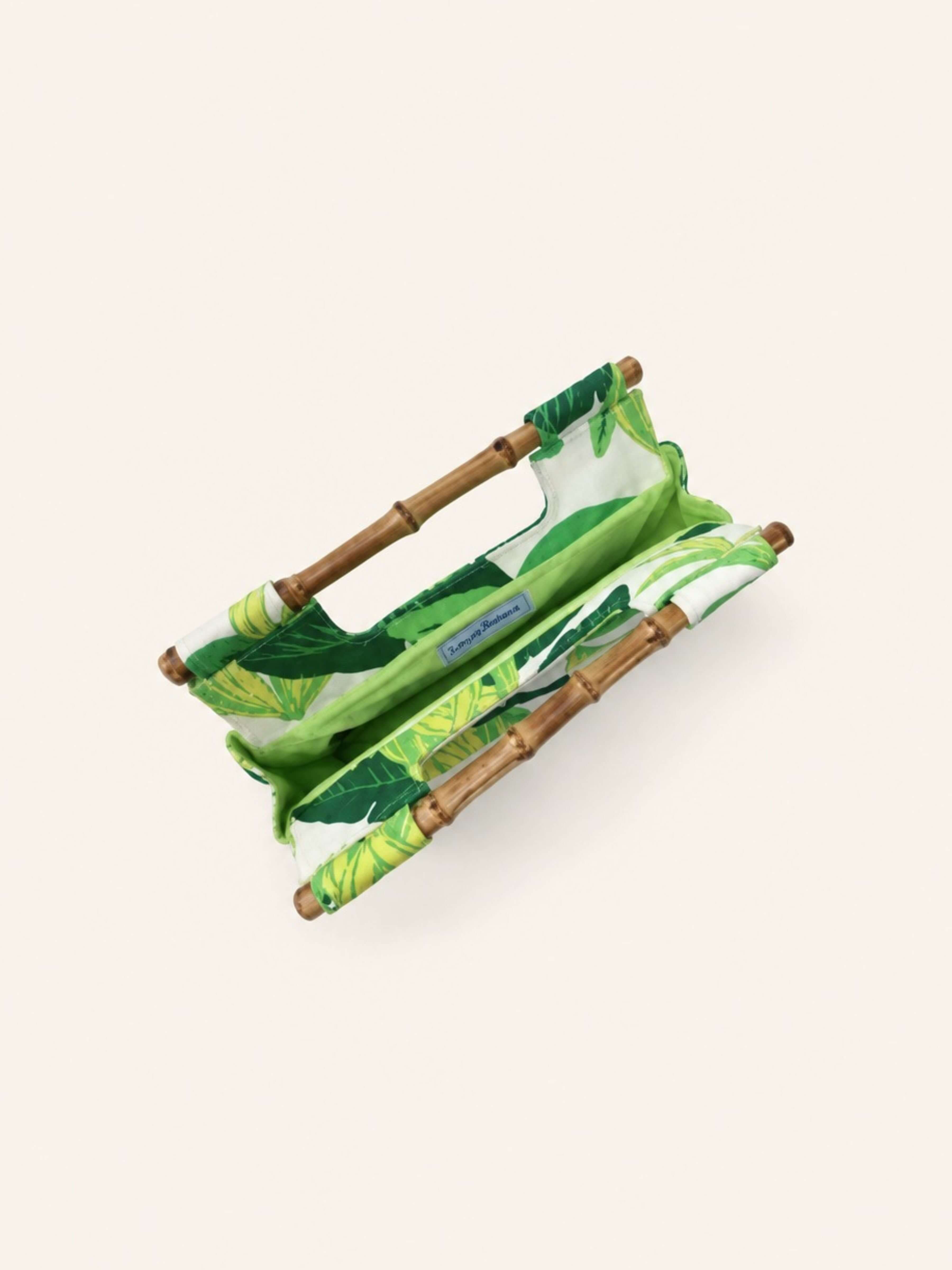 A compact folding camp chair with a green tropical leaf print fabric and natural bamboo-style wooden frame, shown on a solid light beige background.
