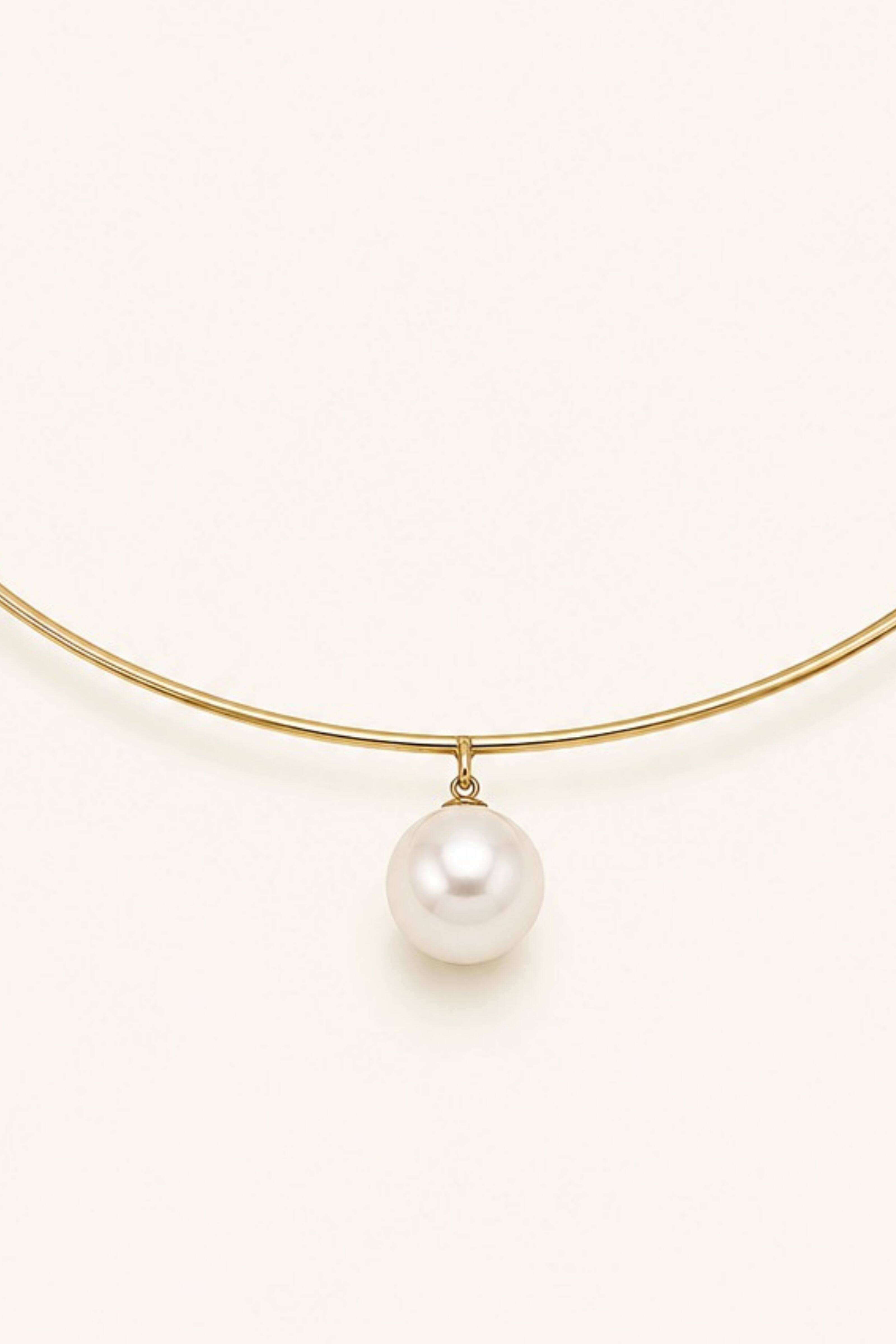 A delicate gold wire necklace featuring a single white freshwater pearl pendant, photographed against a solid, warm off-white background.