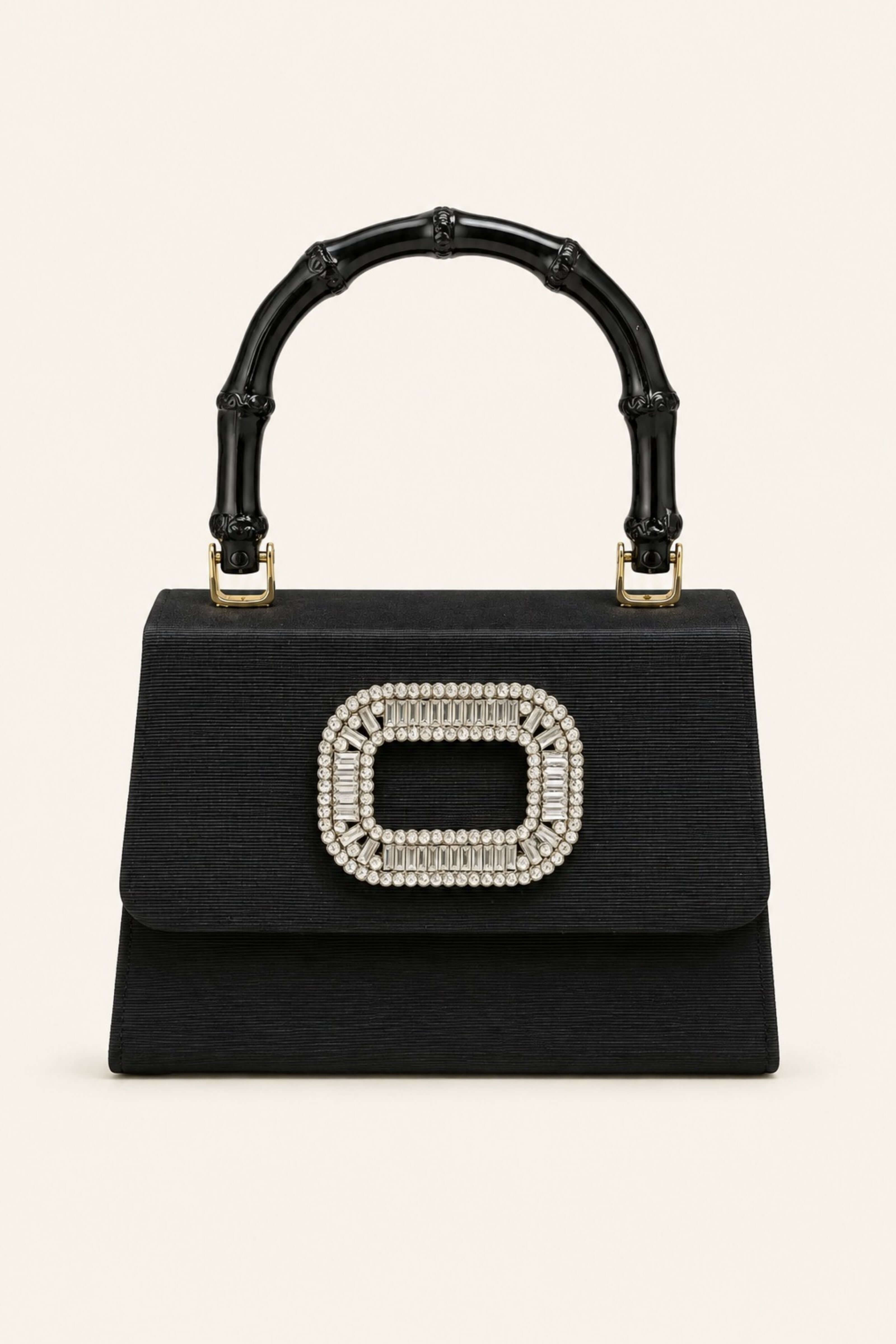 A black structured handbag with a bamboo-style top handle and a large rectangular rhinestone embellishment on the front flap, shown against a plain light beige background.