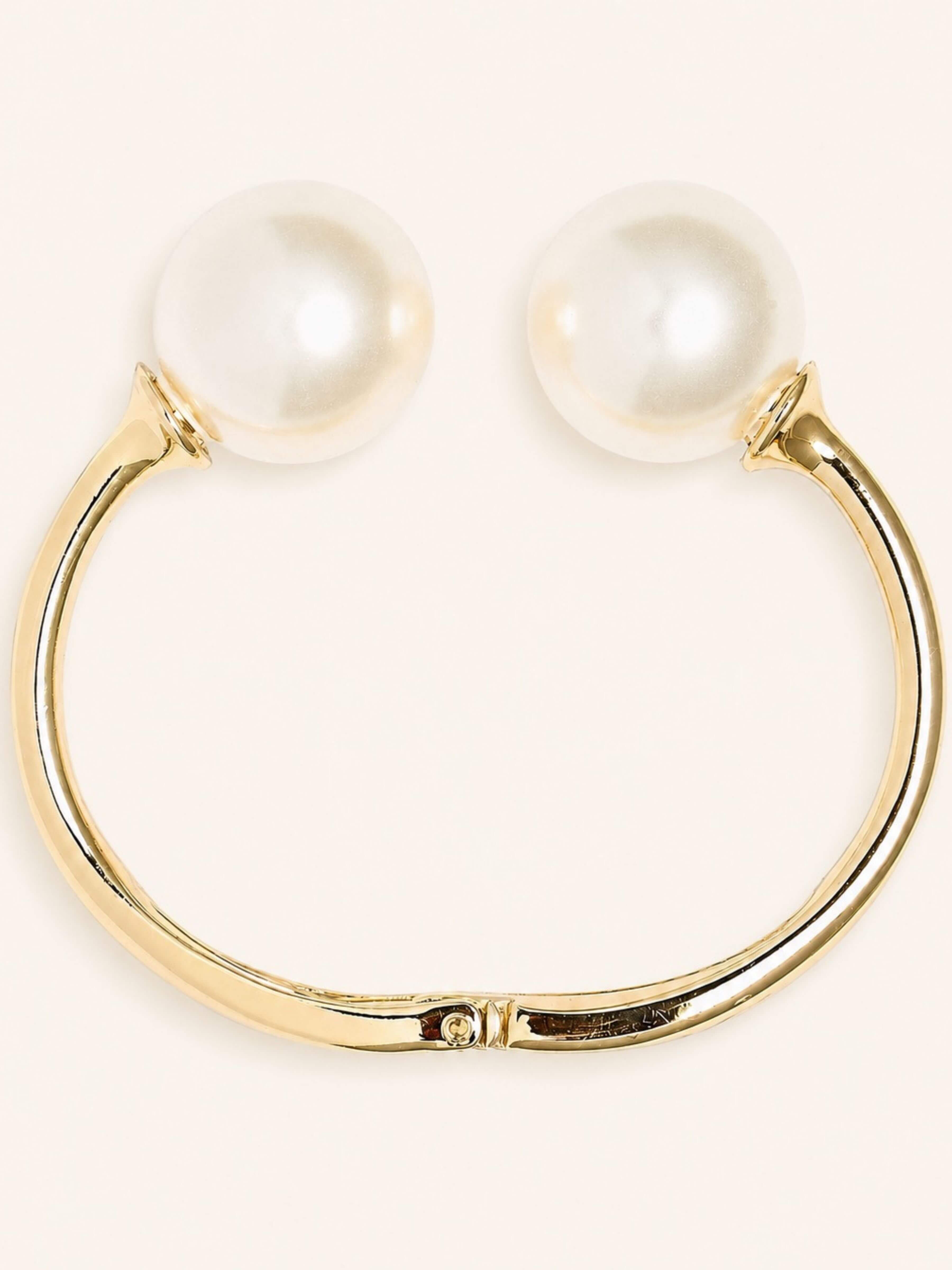 Gold-tone hoop earring with two large white pearl-like round studs, shown on a plain light beige background.