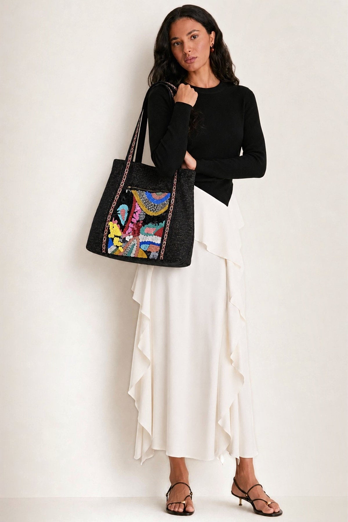 The Black Triple Entry Embellished Shoulder Bag carried on the shoulder with a black sweater and a long white ruffled skirt.