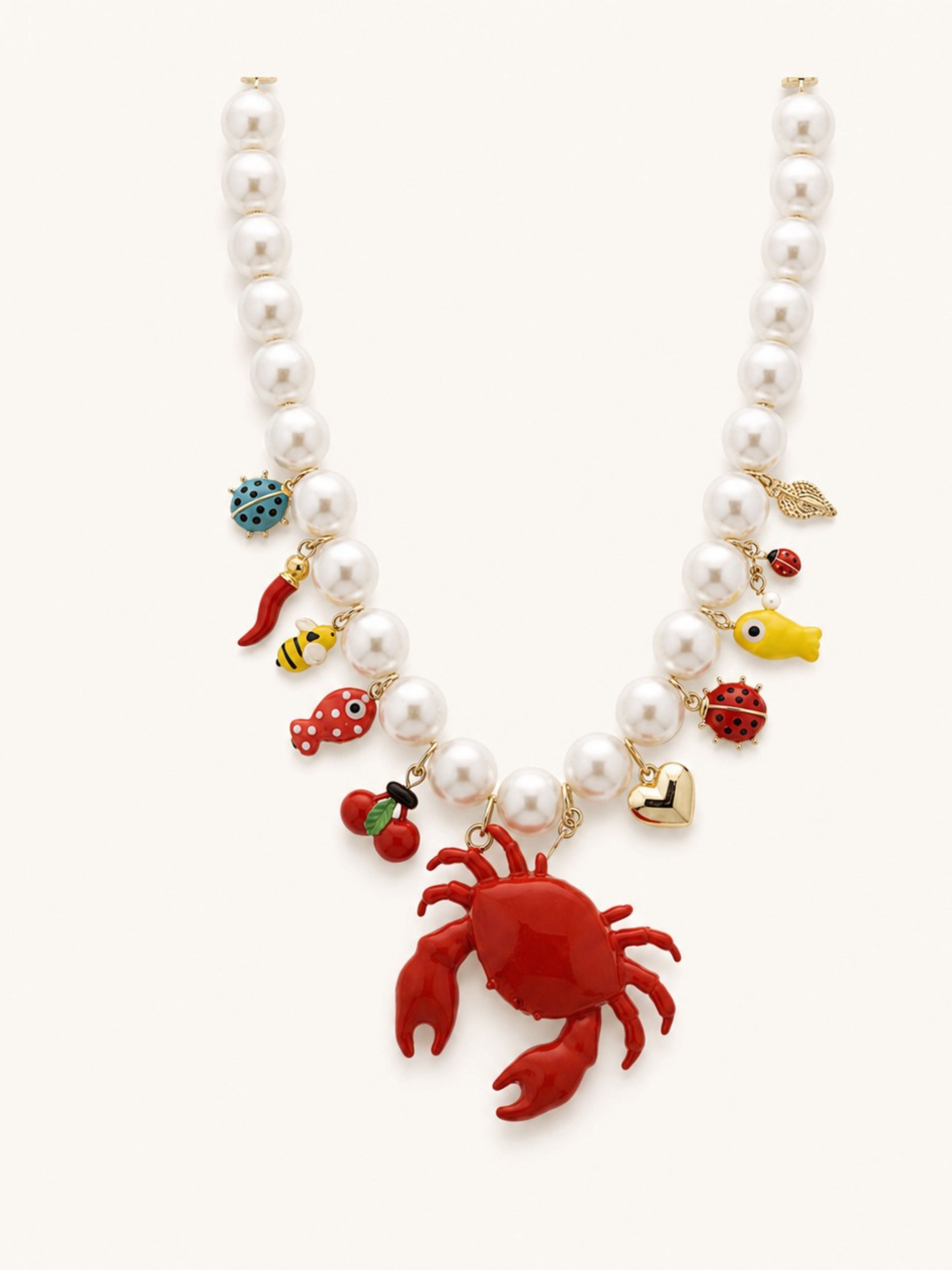 A pearl beaded necklace with a red lobster pendant and colorful sea-themed charms including a yellow fish, red lobster, cherry, ladybug, and gold heart on a light cream background.