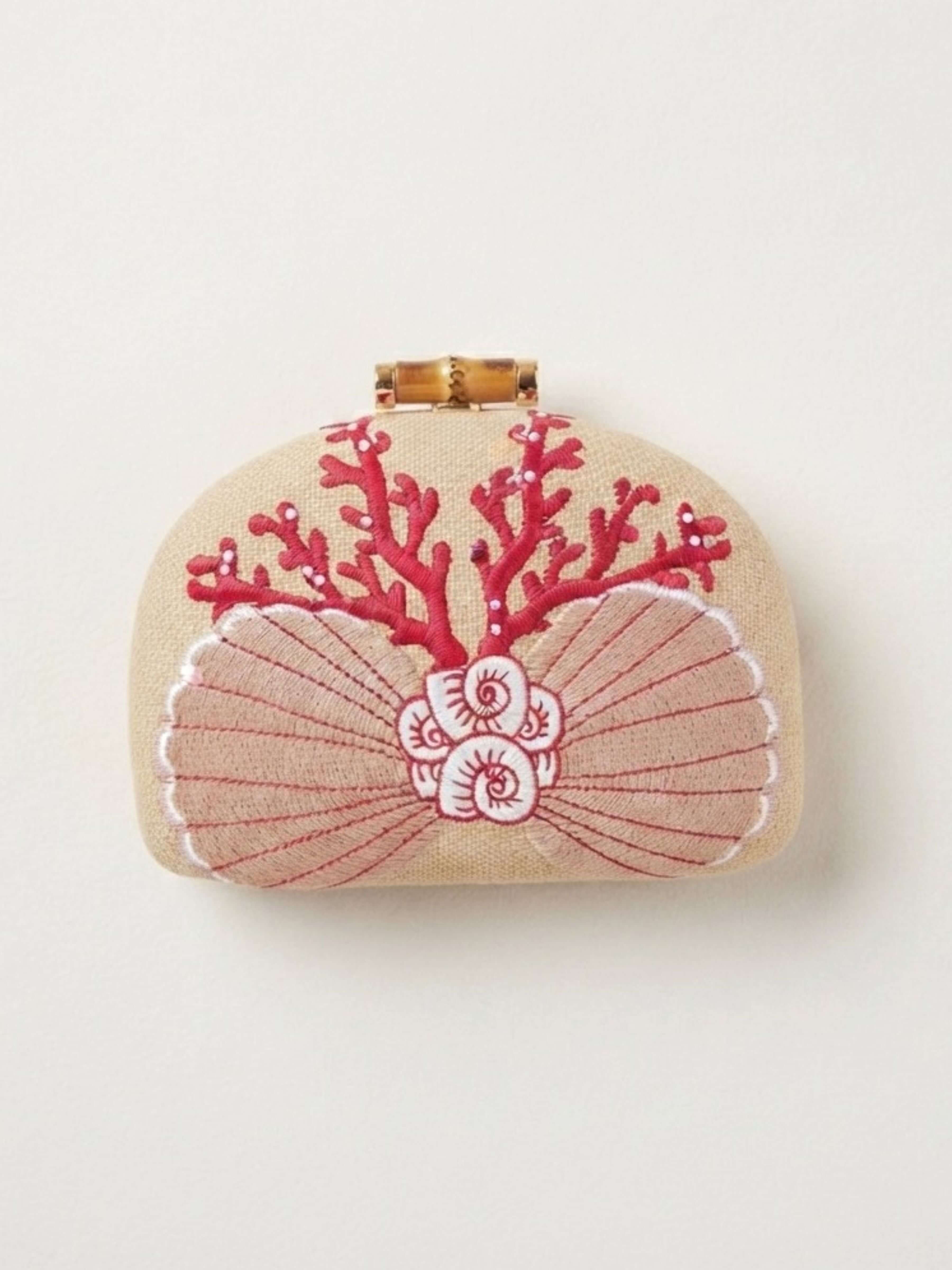 A small beige clutch bag with a bamboo-style clasp, decorated with red coral and pink seashell embroidery on a plain off-white background.