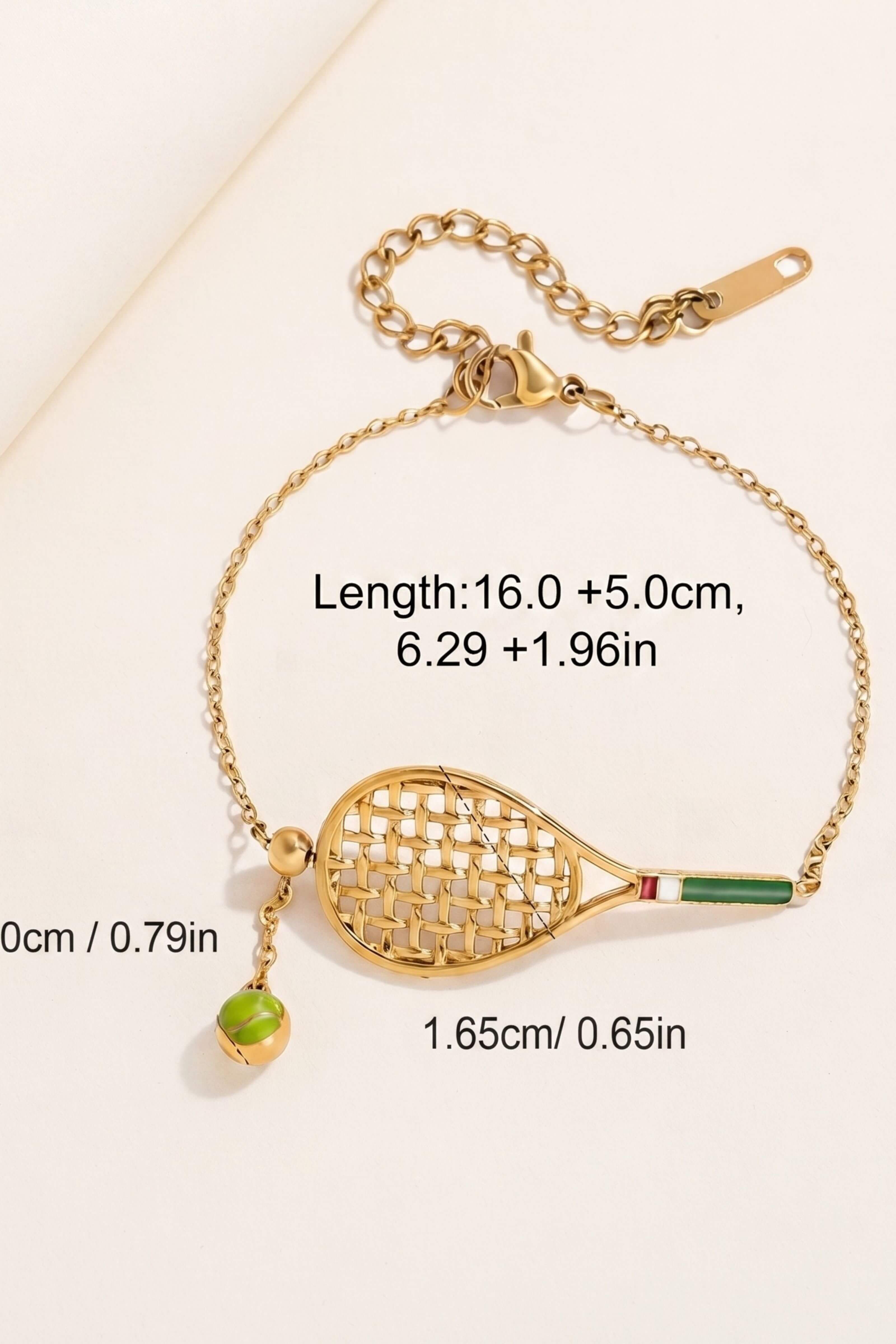 Gold tennis racket charm bracelet with a small green bead dangling from the side, shown on a light beige background with printed measurements and dimensions.