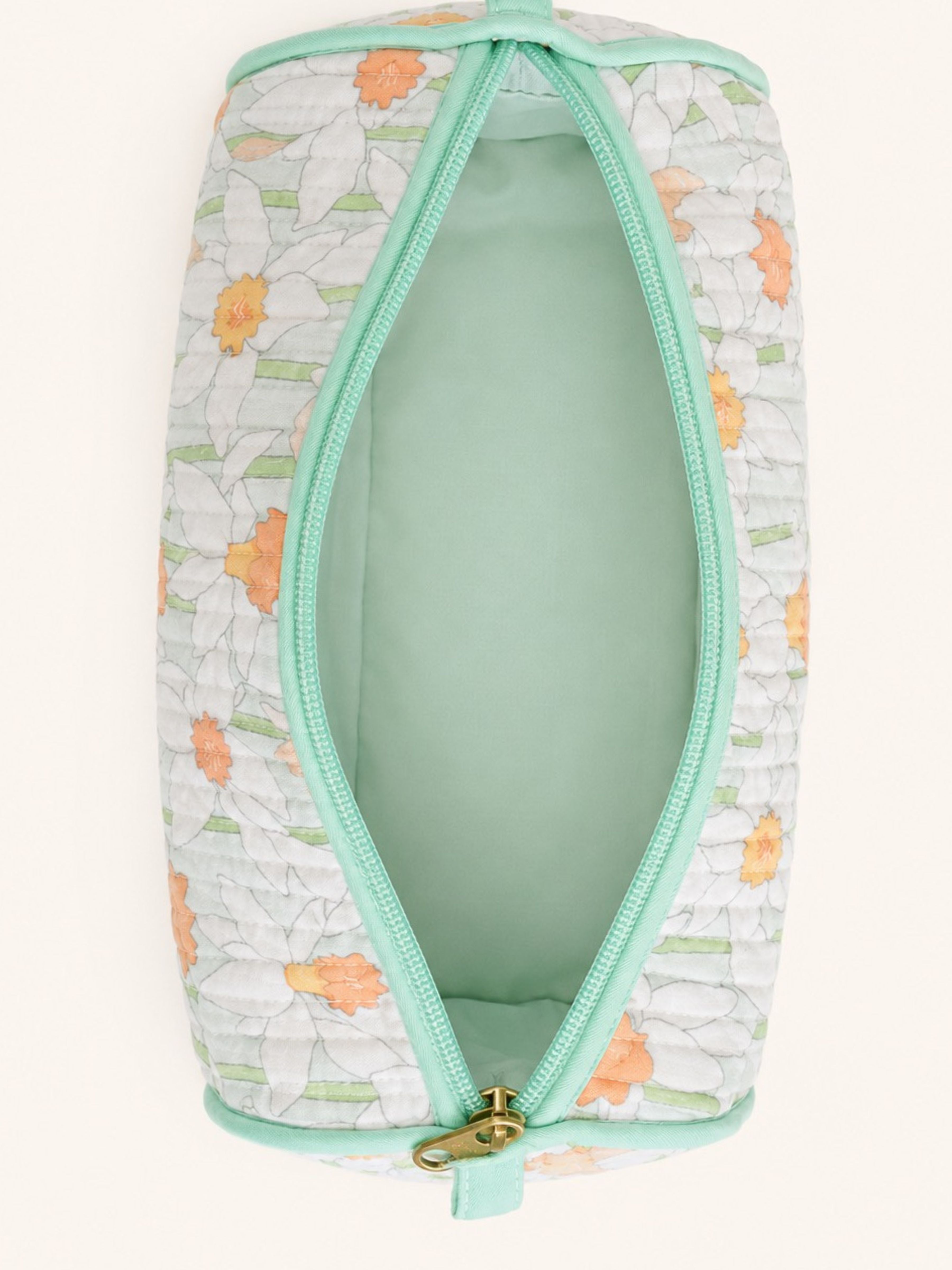 A quilted cosmetic pouch with a white background, orange and green floral pattern, and mint green trim, shown open to reveal a mint green interior.