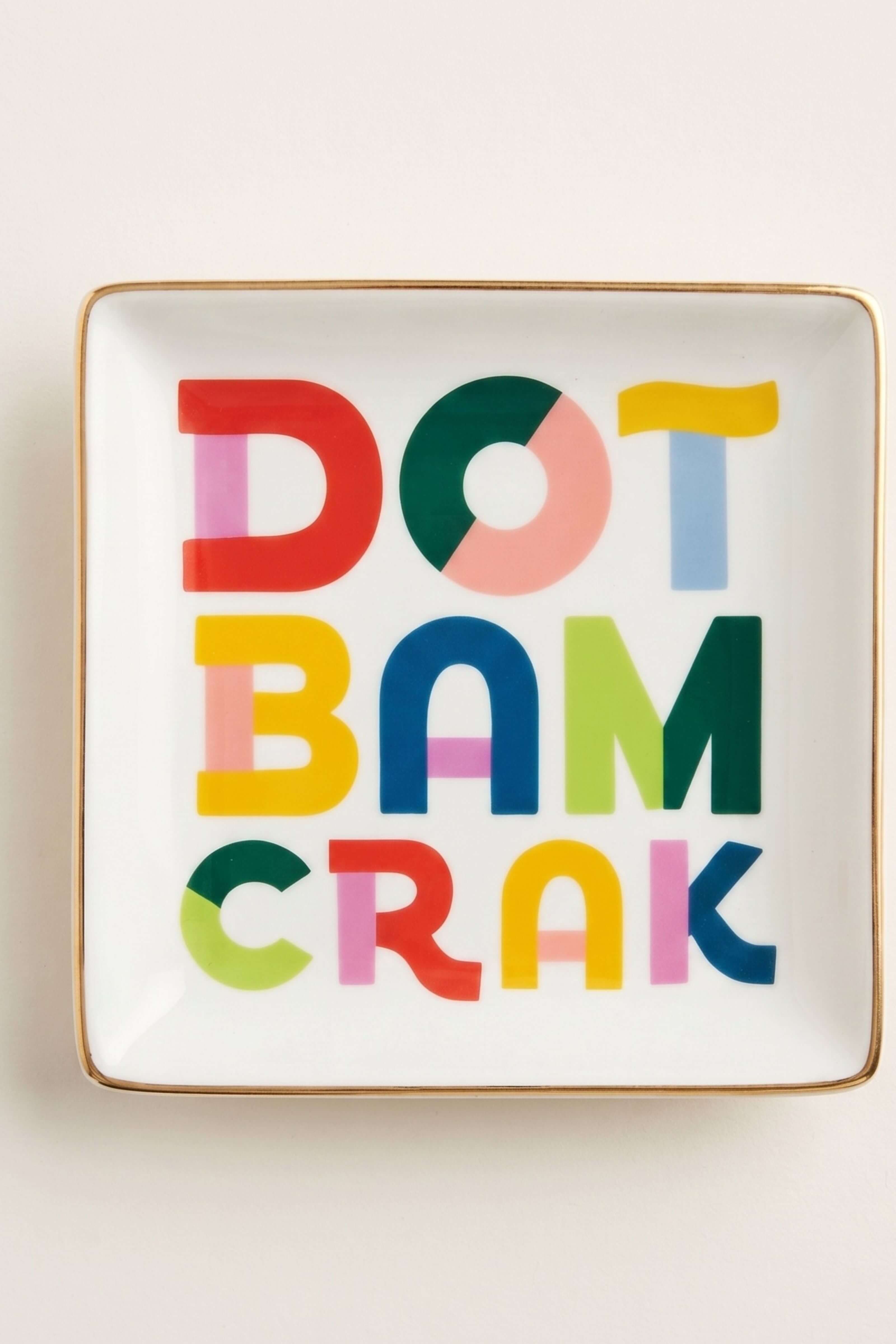 A square white ceramic plate with a gold rim, featuring the phrase 'DOT BAM CRAK' in large, colorful letters with varying dot patterns, set against a plain light background.