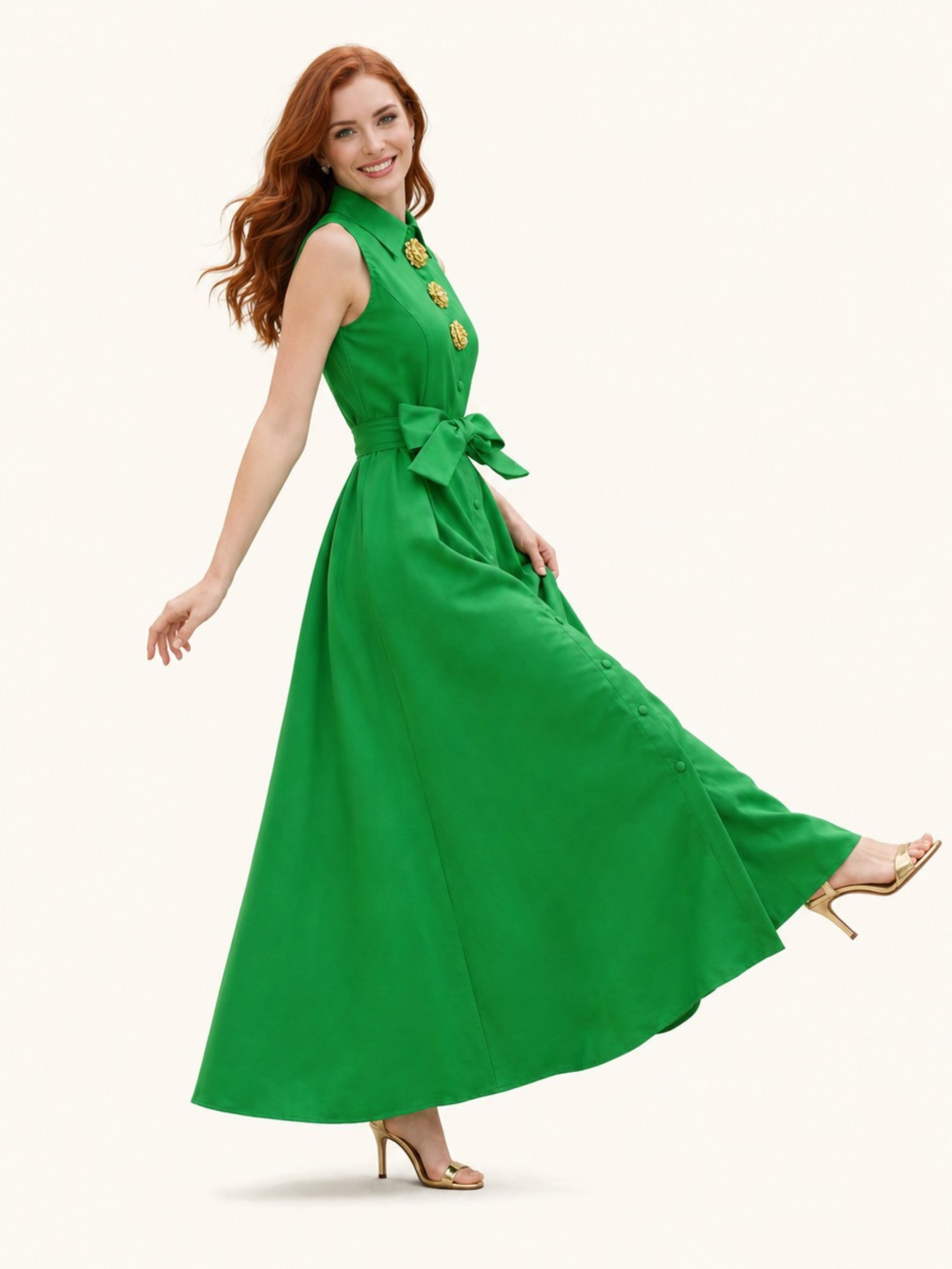A woman modeling a sleeveless green maxi dress with a high collar, gold decorative buttons, a matching waist tie, and a flowing skirt, posed against a solid off-white background.