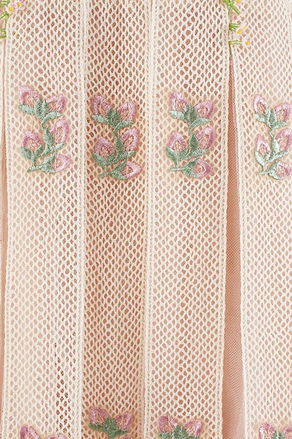Close-up of a light pink pleated mesh fabric with vertical folds and embroidered pink floral motifs with green stems.