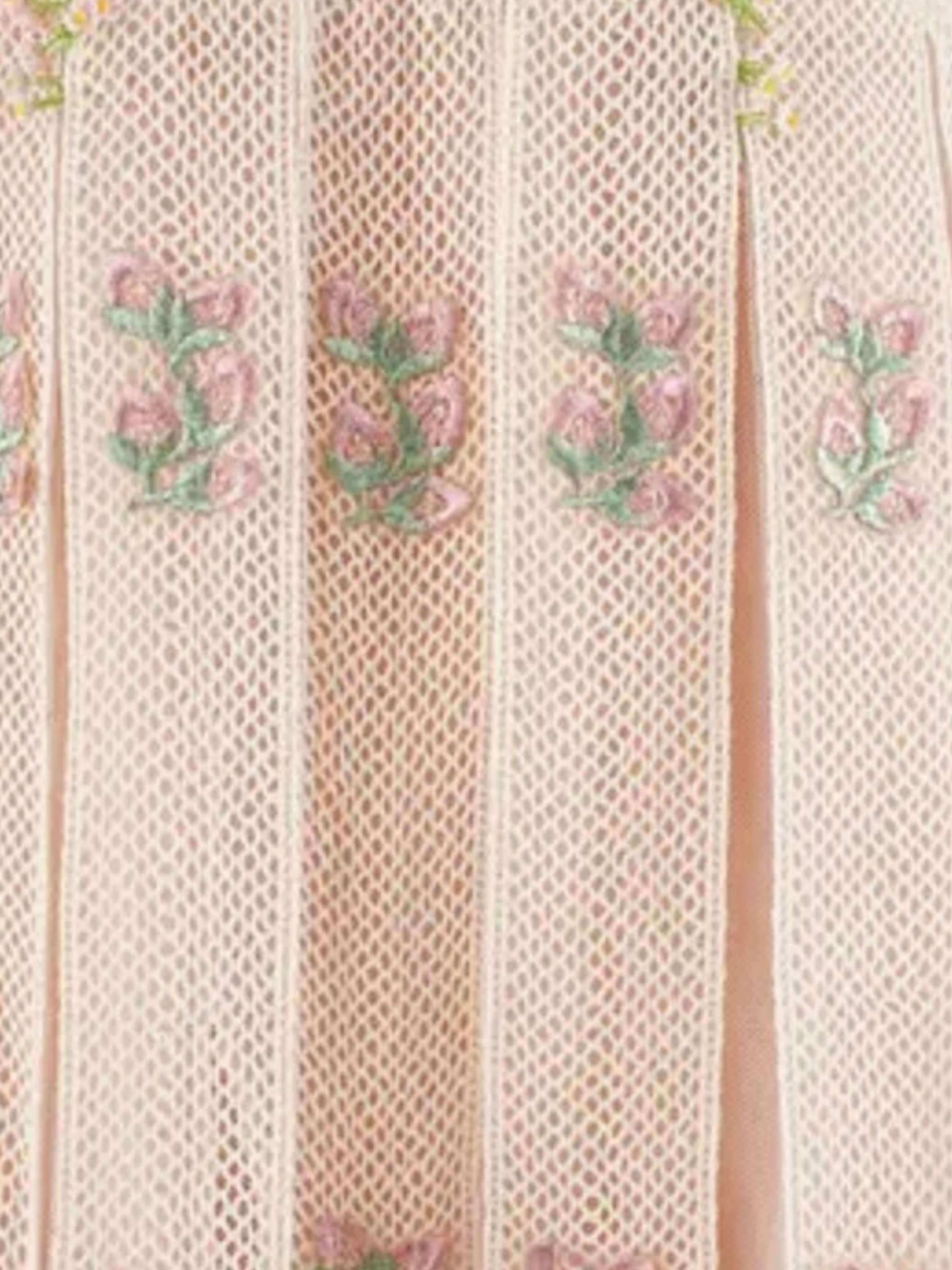Close-up of a light pink pleated mesh fabric with vertical folds and embroidered pink floral motifs with green stems.