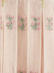 Close-up of a light pink pleated mesh fabric with vertical folds and embroidered pink floral motifs with green stems.