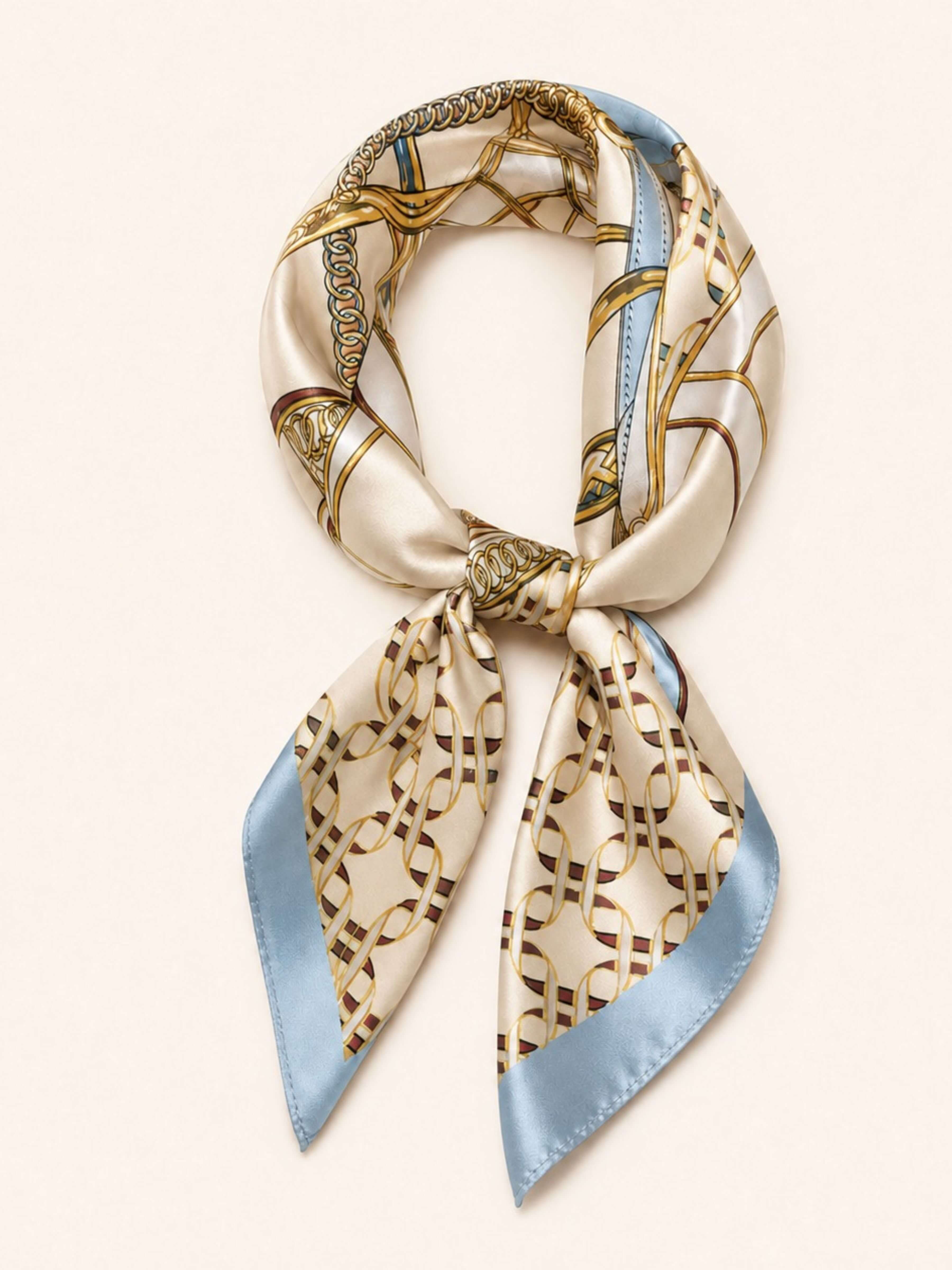 A silk scarf with a beige and gold geometric chain-link pattern and light blue edges, tied in a loop on a light cream background.