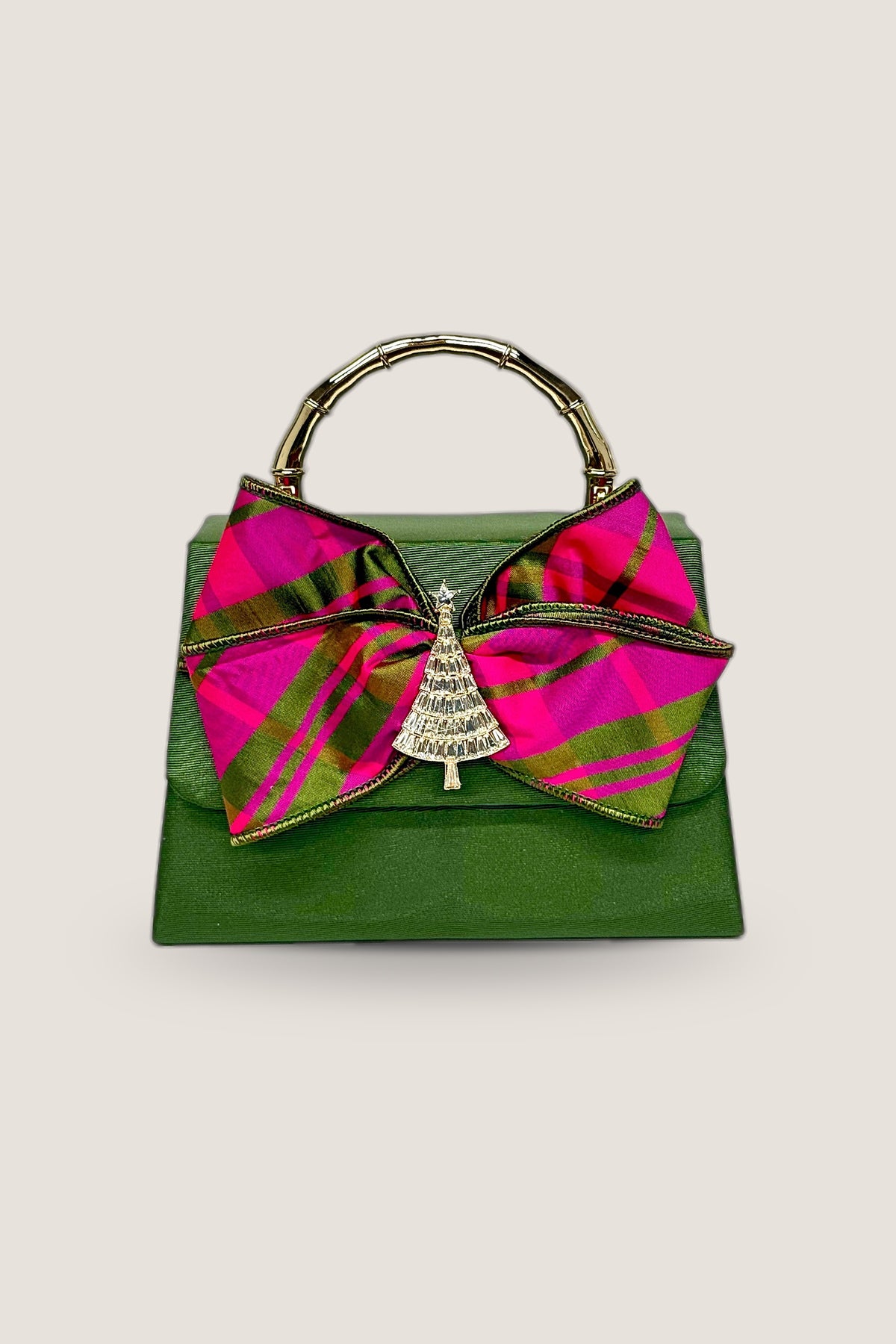 Faille Lulu clutch in green faille with a pink and green plaid bow, rhinestone tree emblem and gold bamboo-style handle, front view on a warm greige backdrop.
