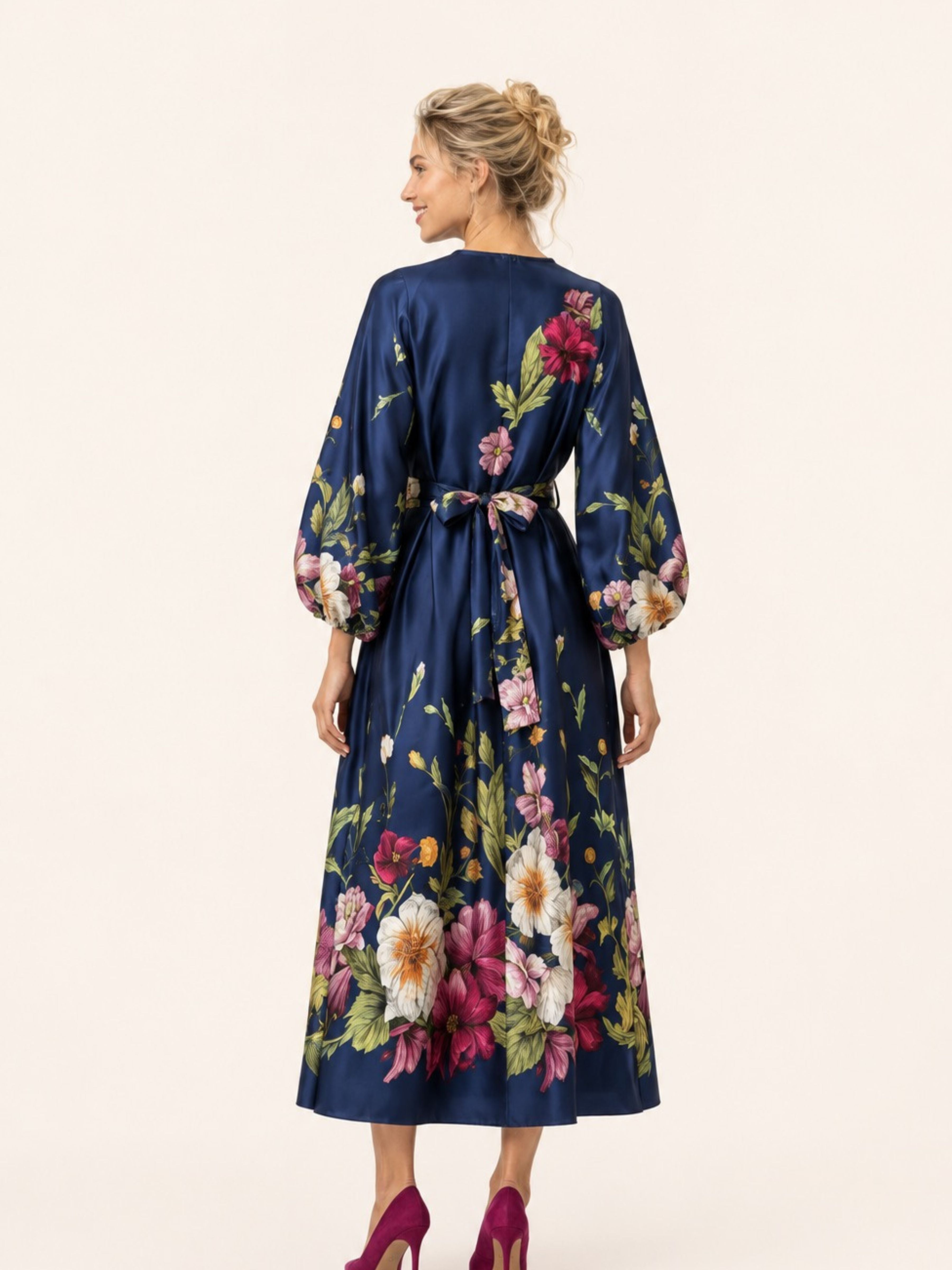 A woman shown from the back wearing a navy blue midi dress with a vibrant multicolor floral print and a tie waist, paired with magenta heels, against a plain cream background.