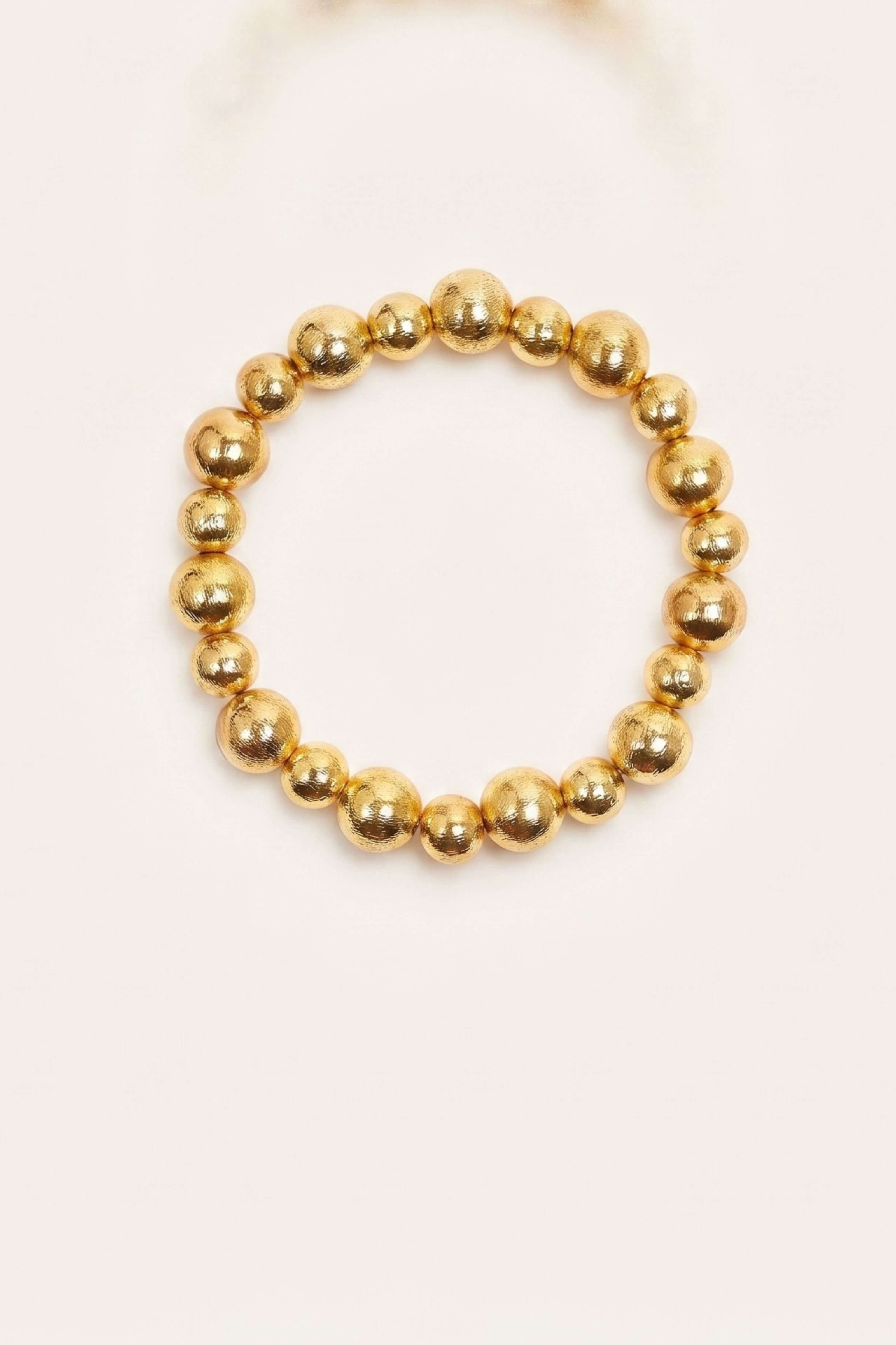 A gold beaded stretch bracelet with polished metallic spherical beads, displayed on a clean off-white background.