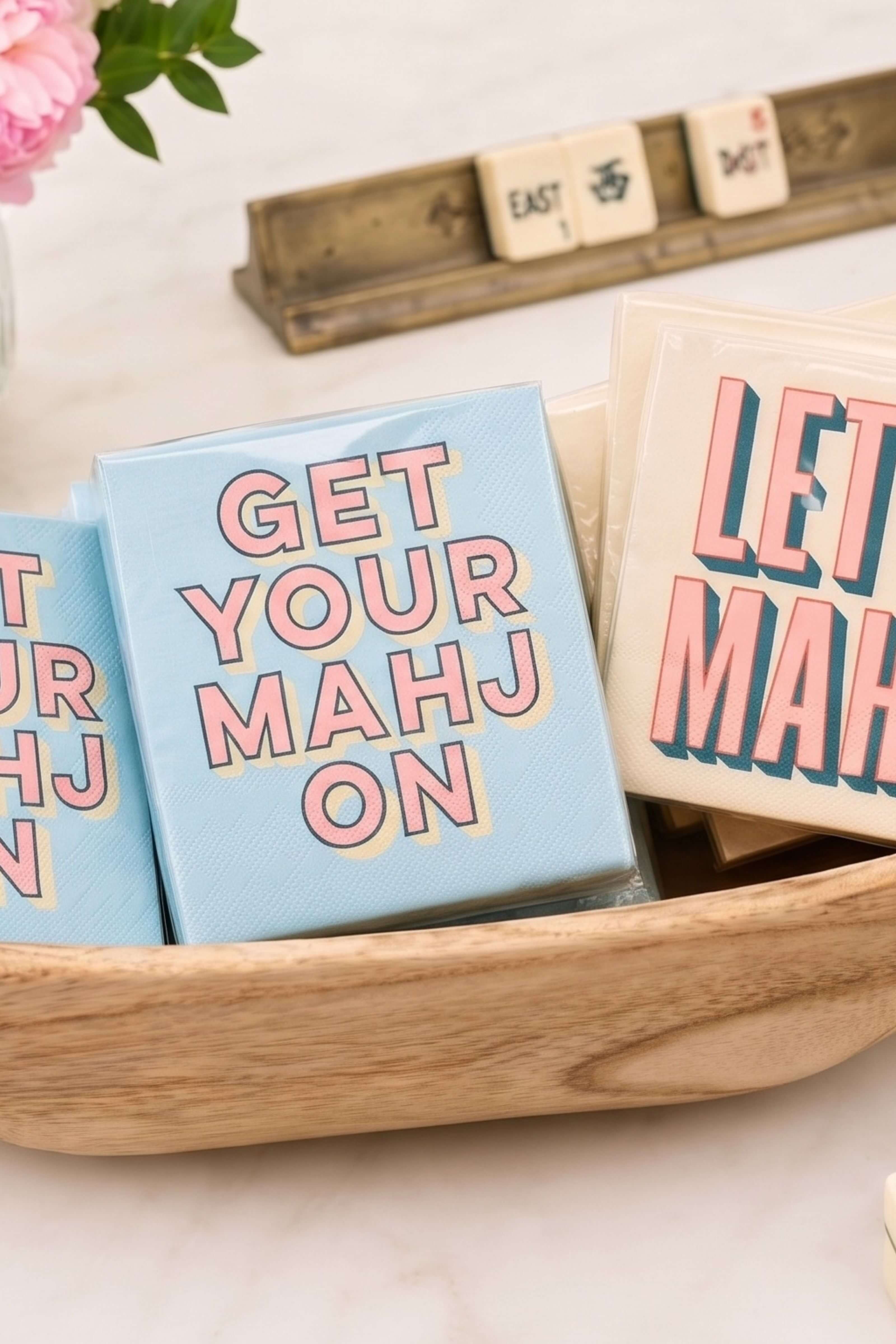 A light blue square card with the phrase 'GET YOUR MAHJ ON' in pink letters outlined in yellow, displayed in a wooden bowl alongside other cards with matching text.